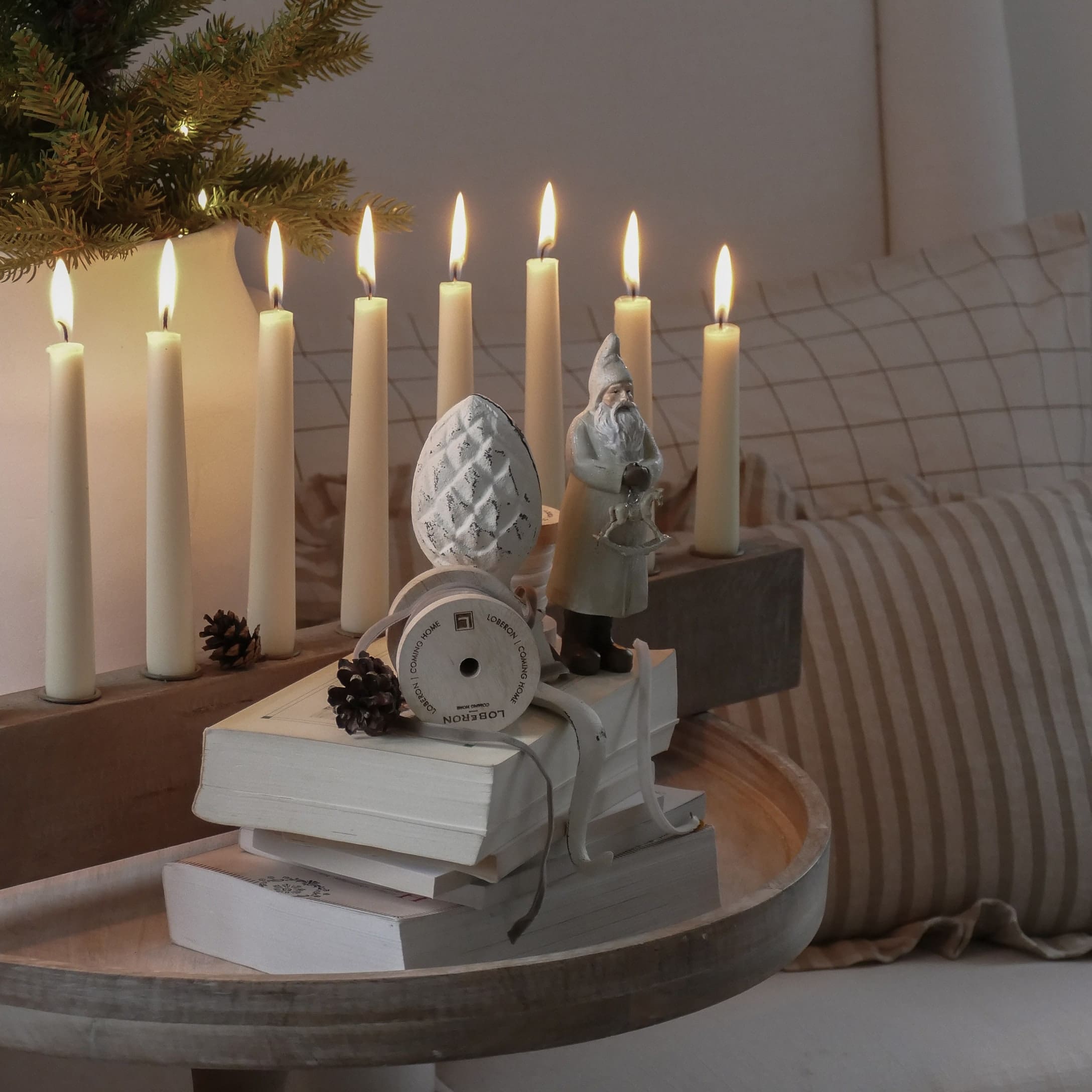 Decorazione natalizia con figura di Babbo Natale, candele accese e libri su vassoio di legno chiaro