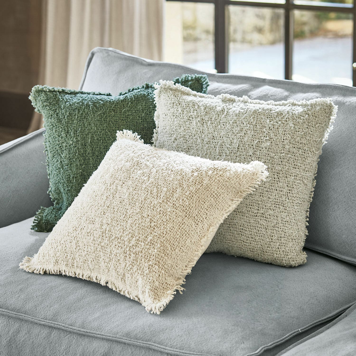 Set di 3 copricuscini Juliana Tre cuscini decorativi in tessuto beige e verde su un divano grigio chiaro