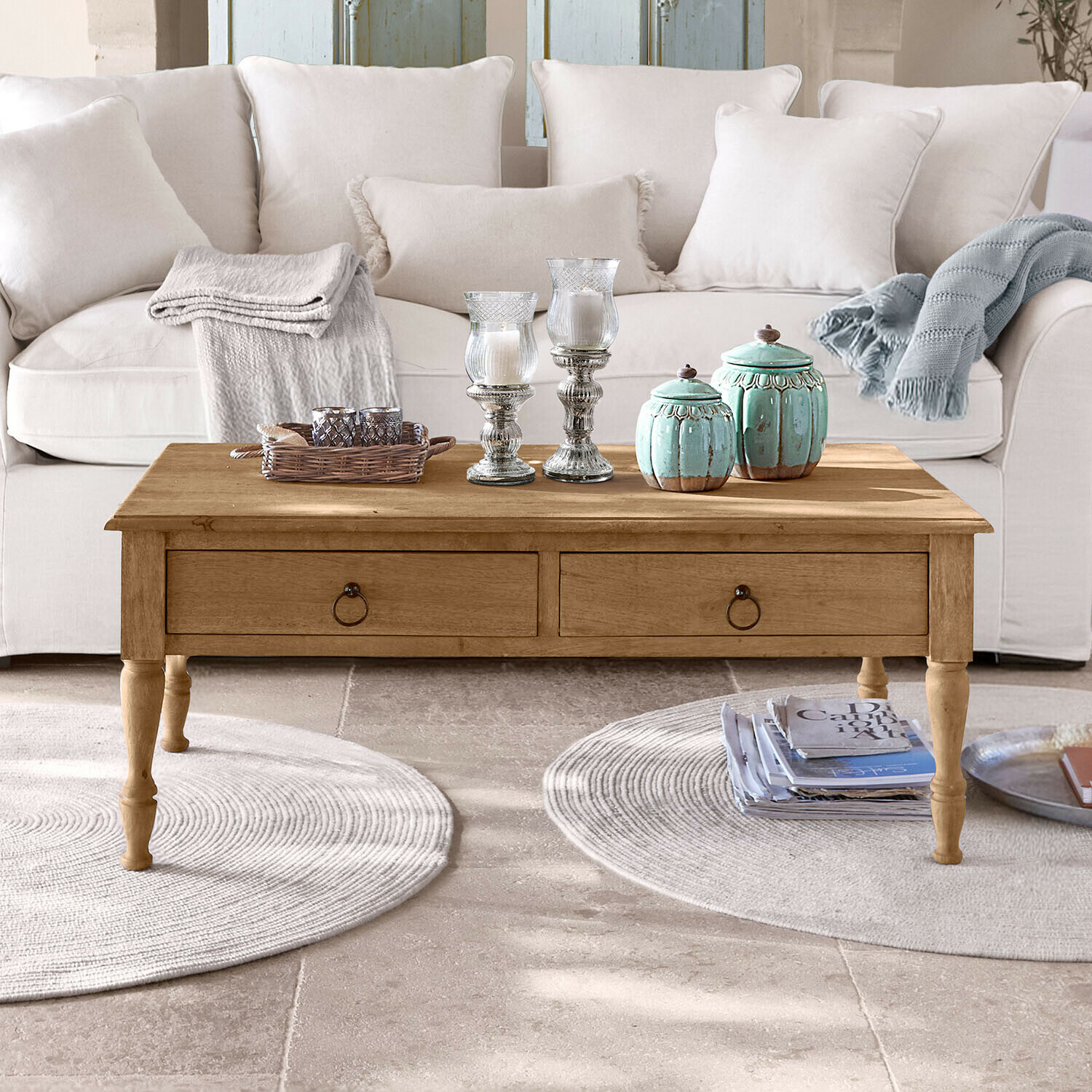 Tavolino in legno con cassetti davanti a divano chiaro, decorazioni e coperte sul piano