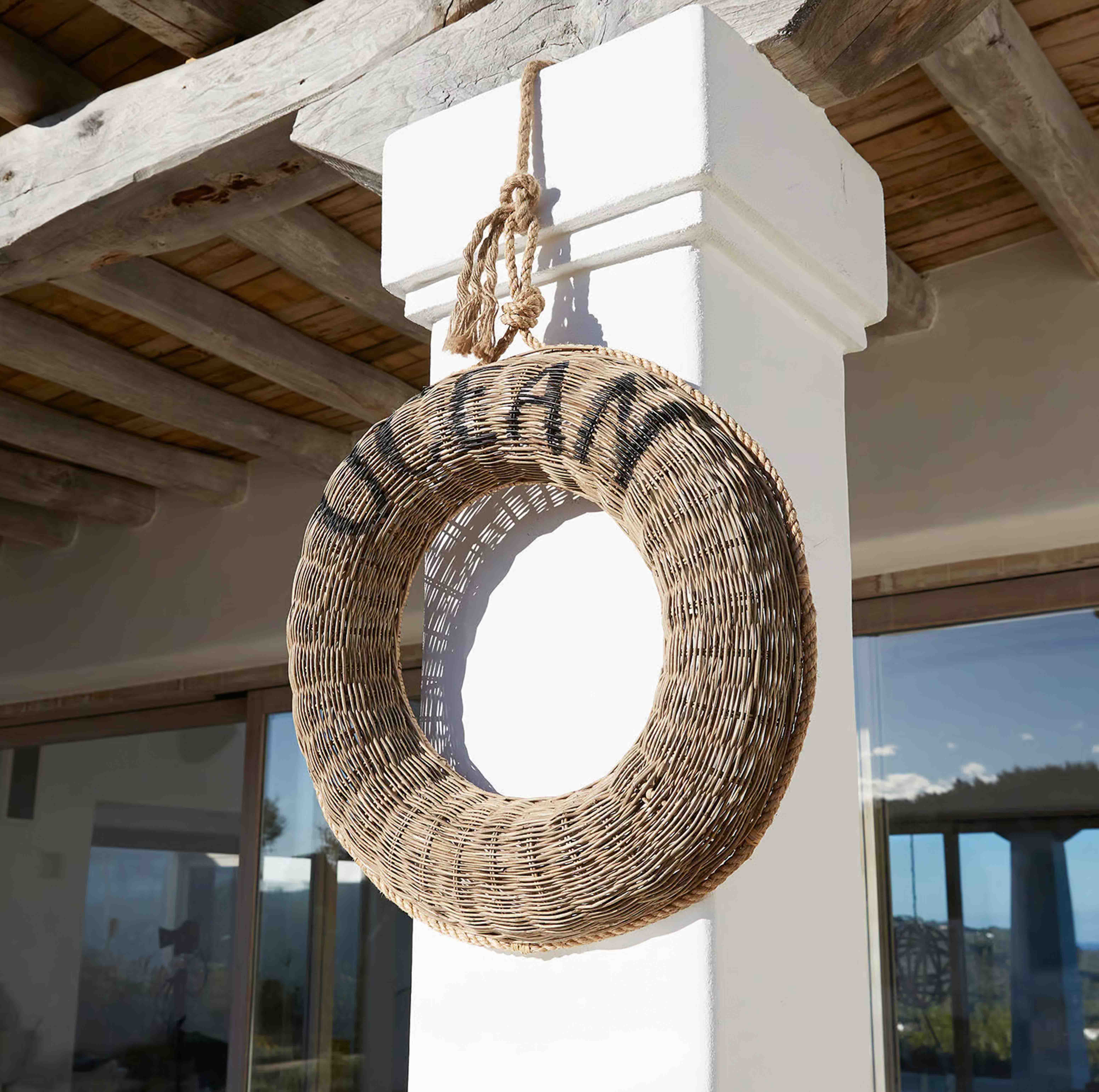 Corona rotonda in vimini naturale appesa a una colonna bianca sotto un soffitto in legno rustico