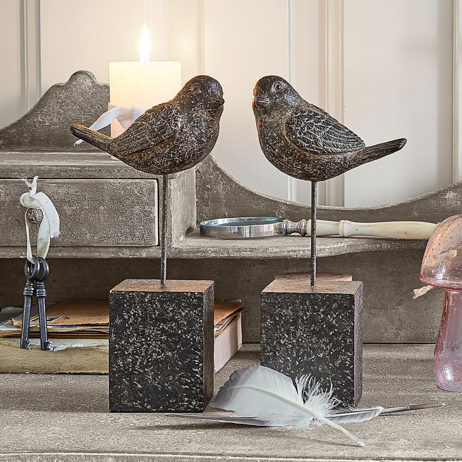 Coppia di uccellini decorativi Juxivel Uccelli decorativi in metallo scuro su basi quadrate su tavolo rustico con piuma bianca