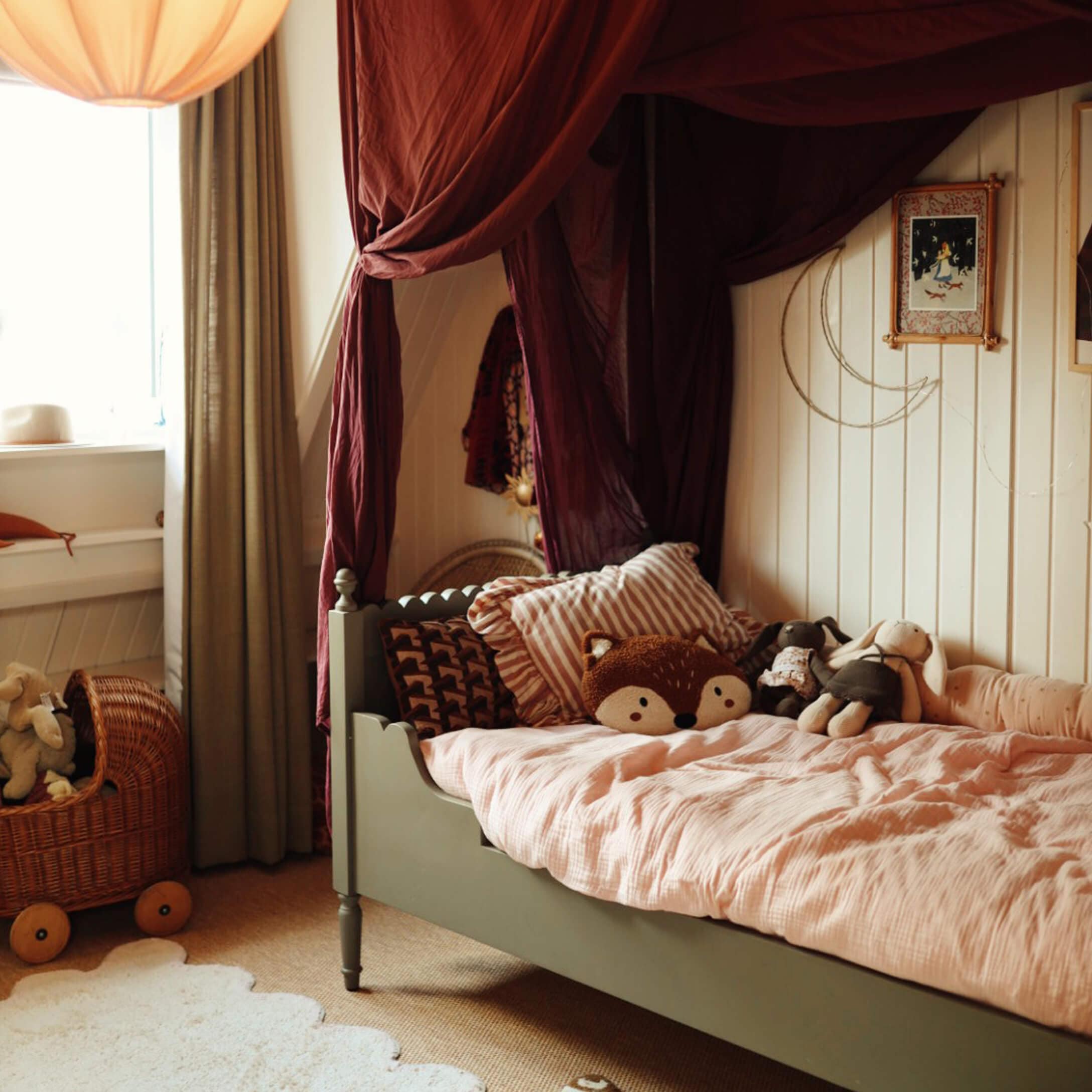 Letto per bambini verde con biancheria rosa e peluche in stanza accogliente con tende bordeaux