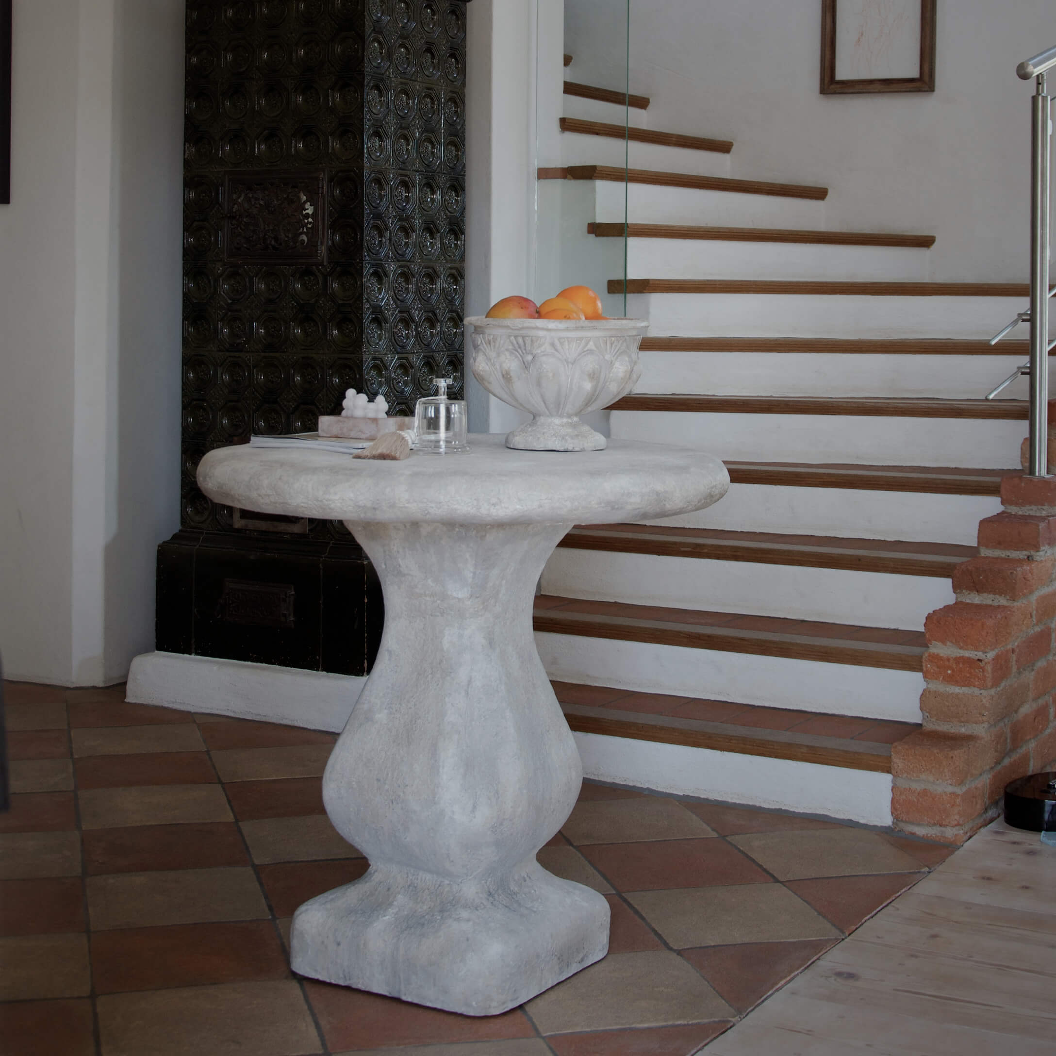 Tavolo rotondo in cemento grigio vicino a scale, ciotola decorativa con frutta sopra
