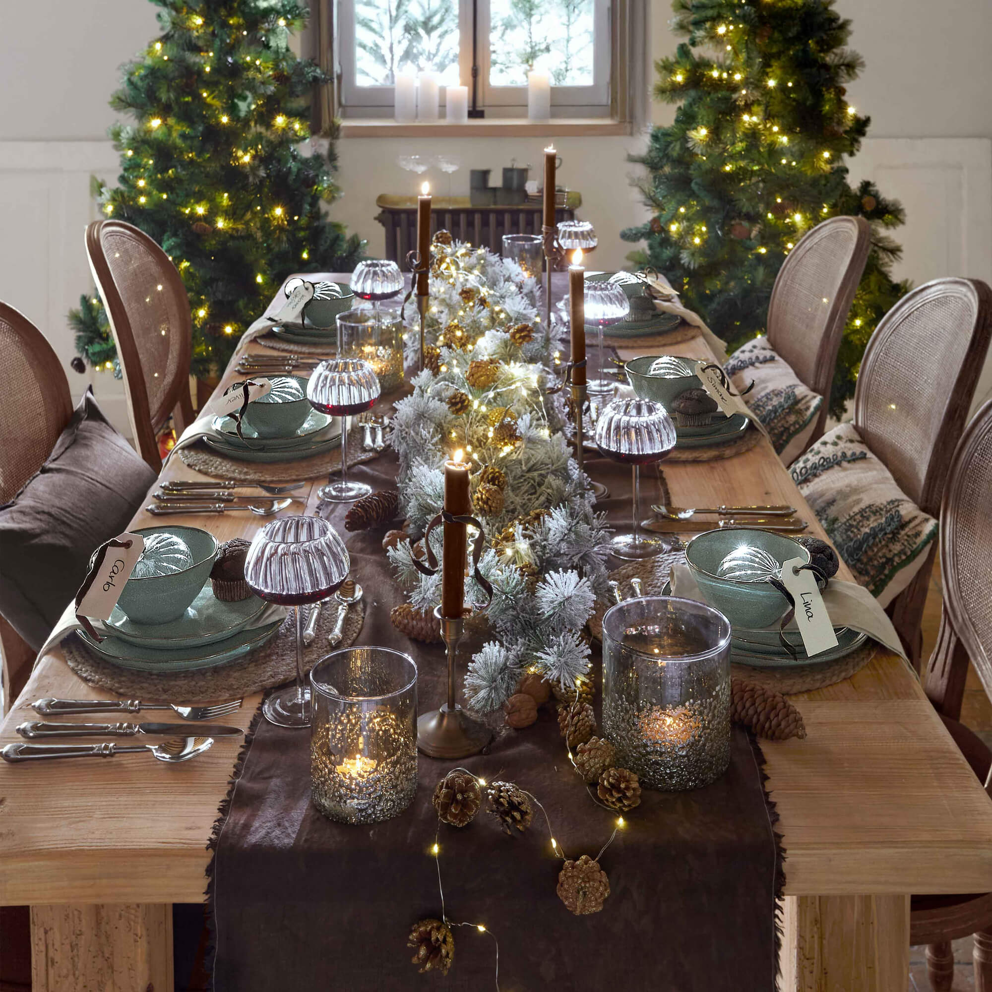 Tavola in legno decorata per Natale con stoviglie verdi, candele e luci LED