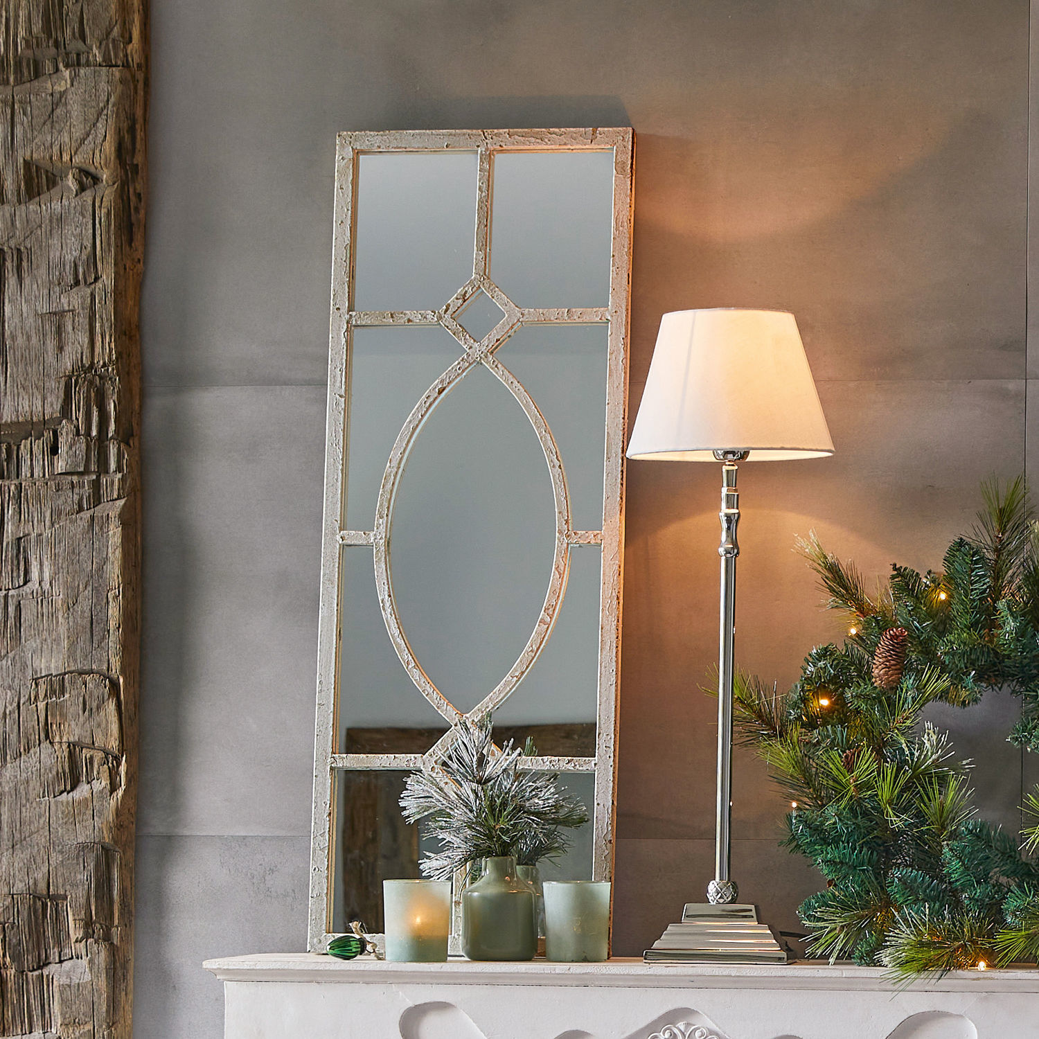 Specchio decorativo con cornice bianca invecchiata su camino con lampada e corona natalizia