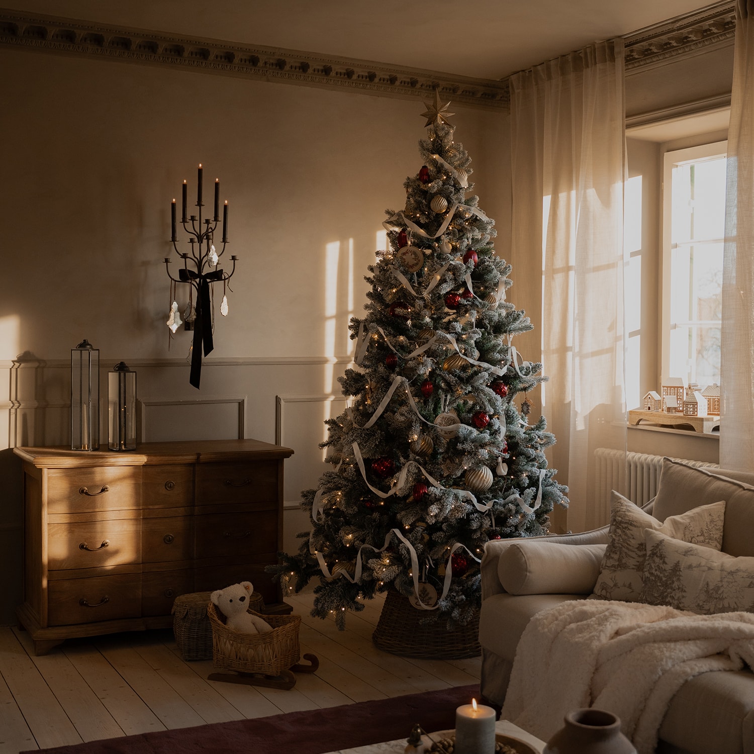 Soggiorno accogliente con albero di Natale innevato decorato con palline rosse e dorate e nastro bianco