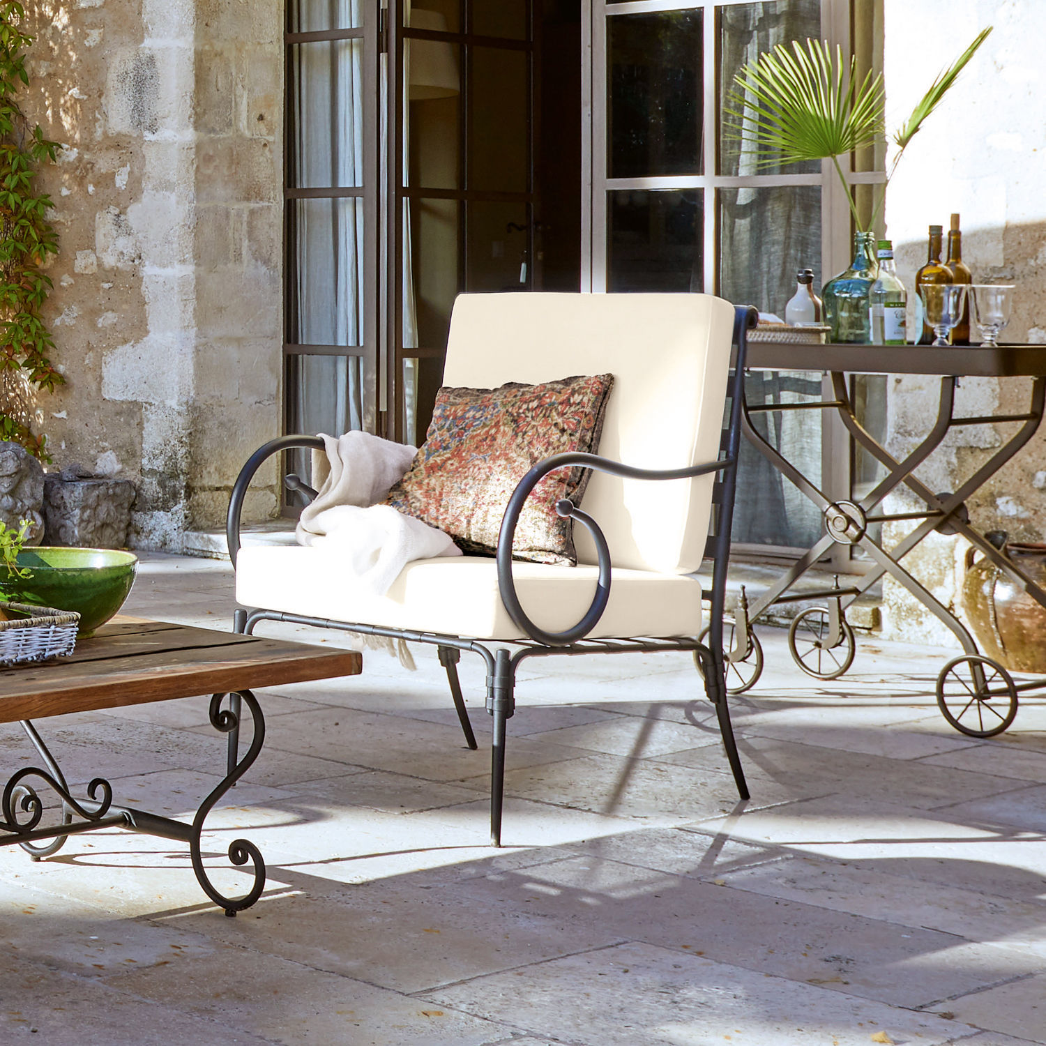 Poltrona Neret Divano da giardino in metallo con cuscini crema e cuscino decorativo su patio in pietra