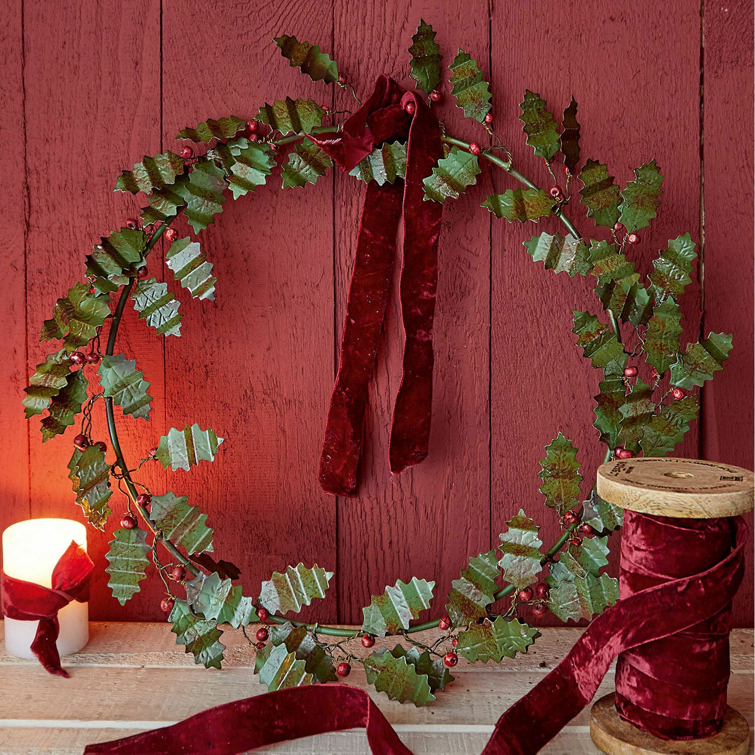 Ghirlanda Fleur Corona decorativa con foglie metalliche verdi e nastro di velluto rosso su sfondo in legno