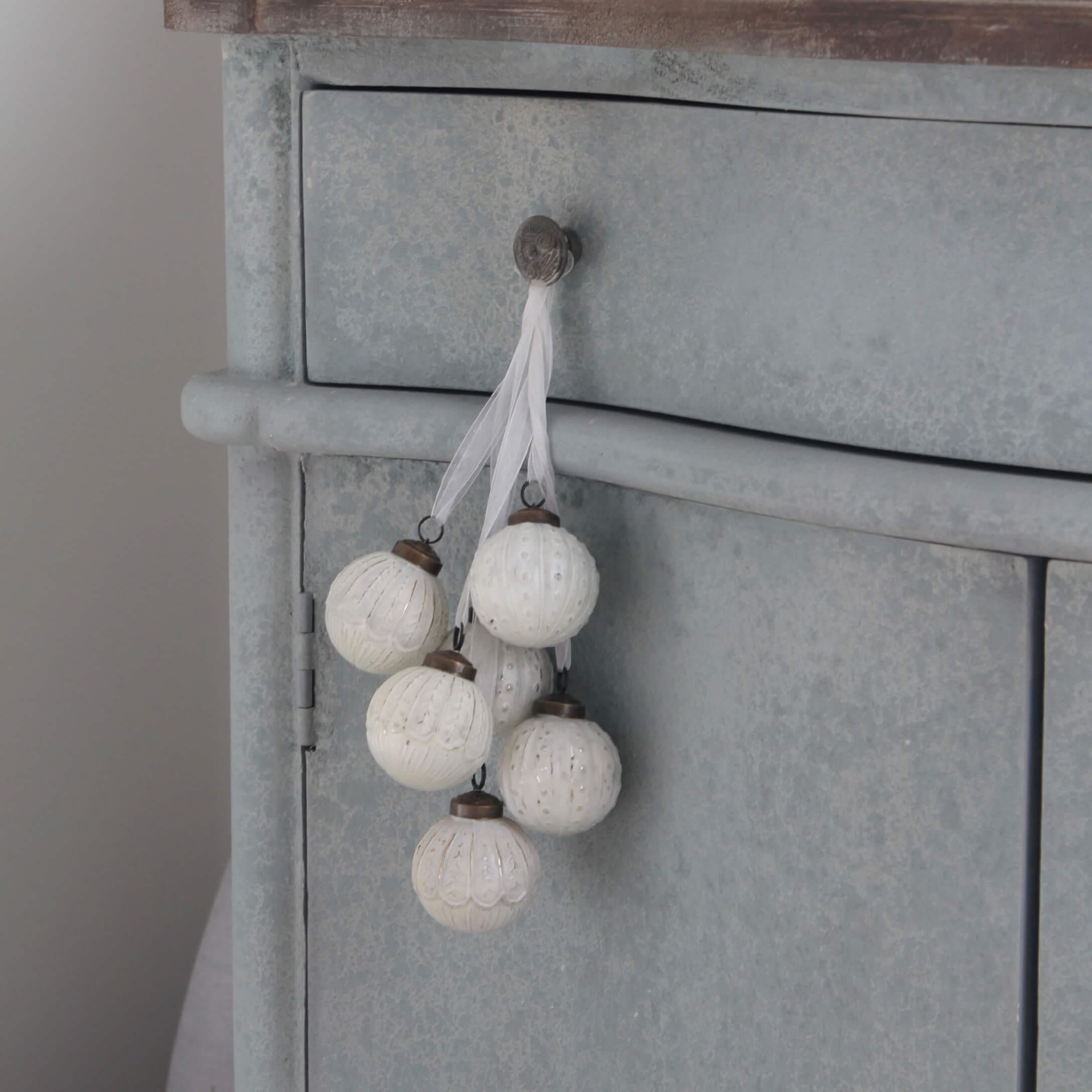 Set di sfere decorative bianche con motivo delicato appese a mobile in metallo grigio