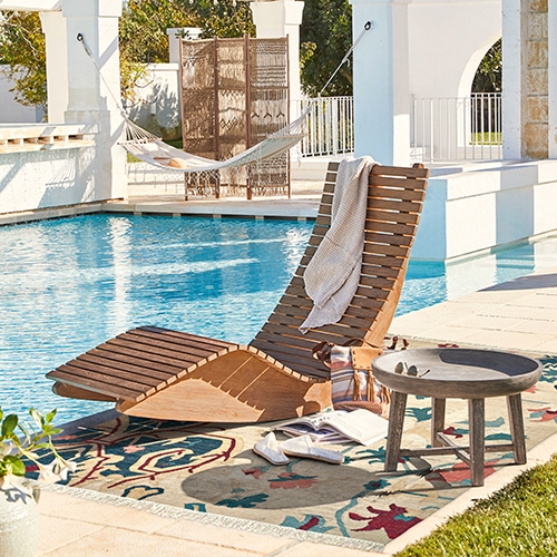 Lettino in legno su terrazza vicino alla piscina con tappeto colorato e tavolino