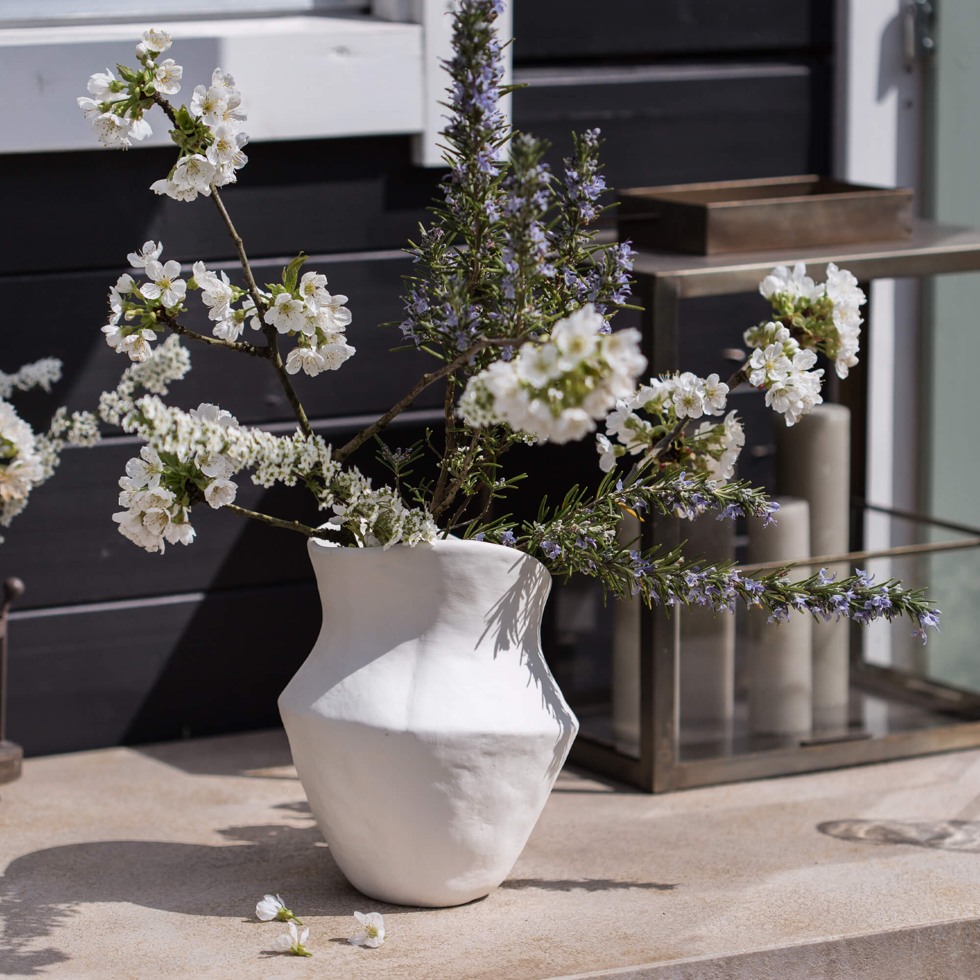 Vaso in ceramica bianca con fiori e rami su tavolo decorativo esterno
