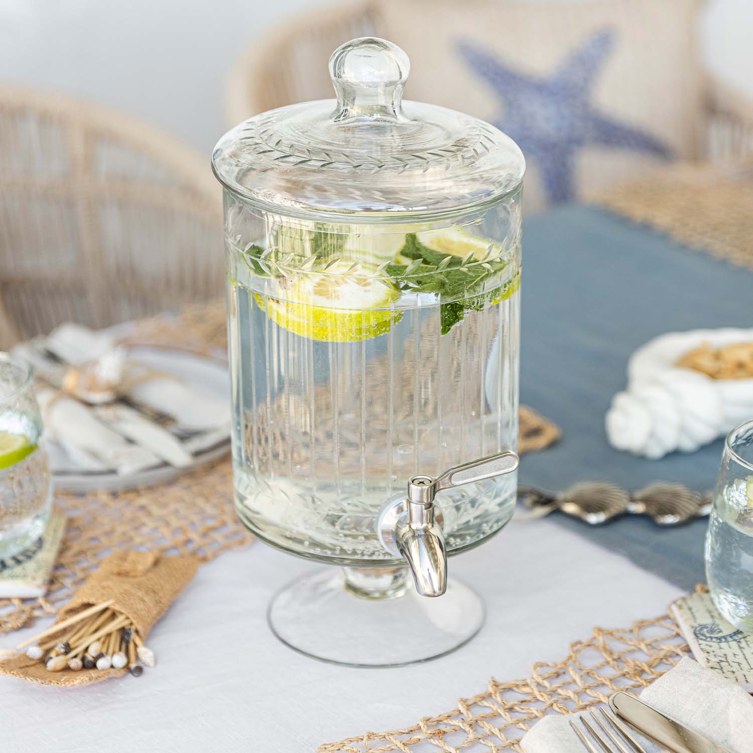 Dispenser per bevande in vetro con coperchio e rubinetto, acqua con limone e menta sul tavolo