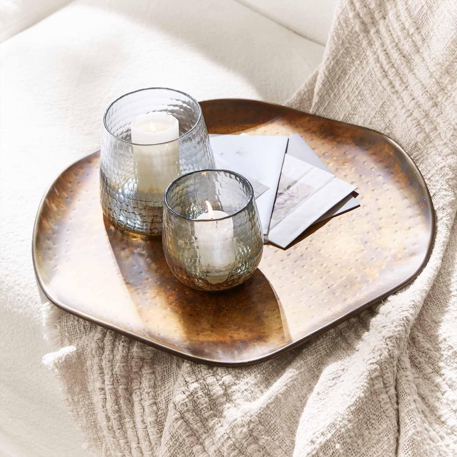 Due lanterne in vetro con candele bianche su un vassoio in rame sopra una coperta chiara per decorazione