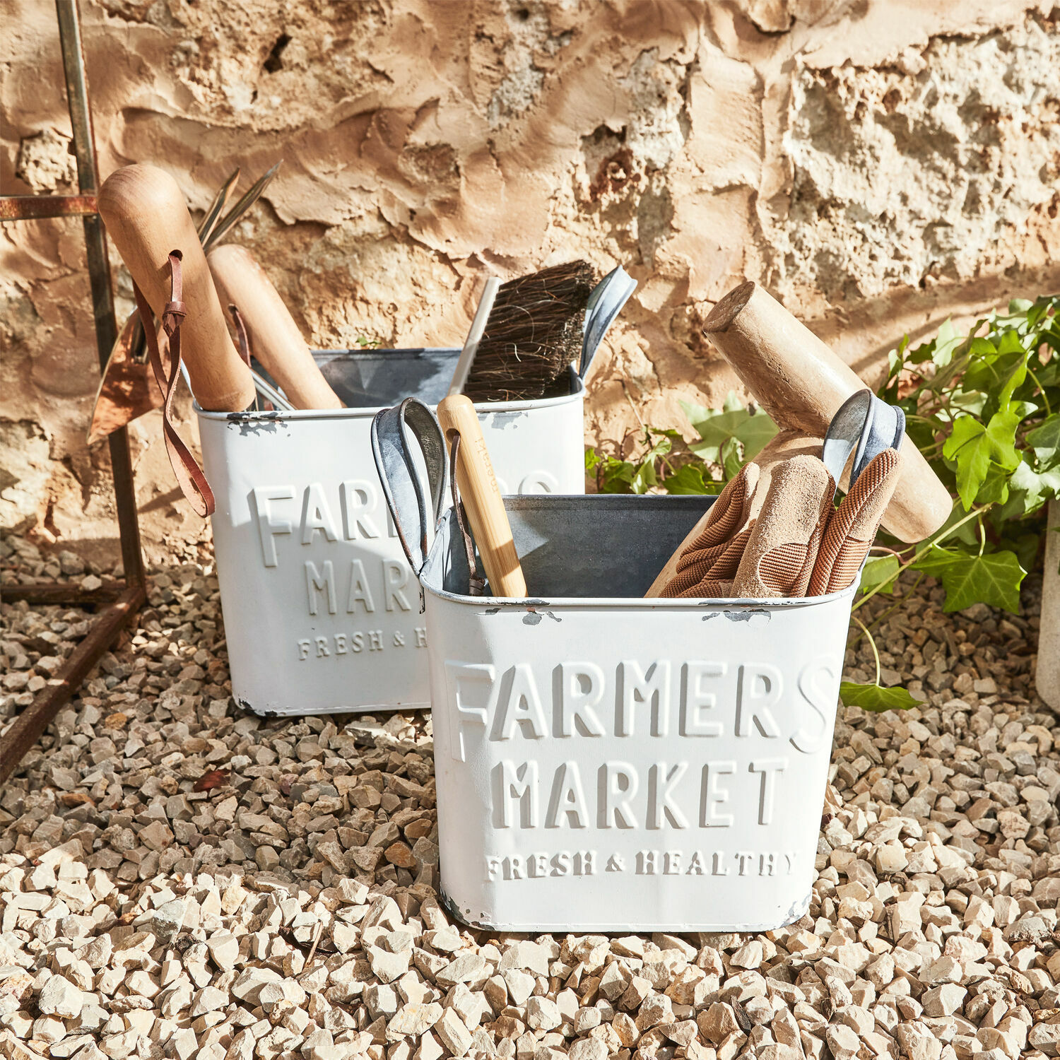 Coppia di contenitori Market Contenitori in metallo bianchi Farmers Market con attrezzi da giardino su superficie ghiaiosa