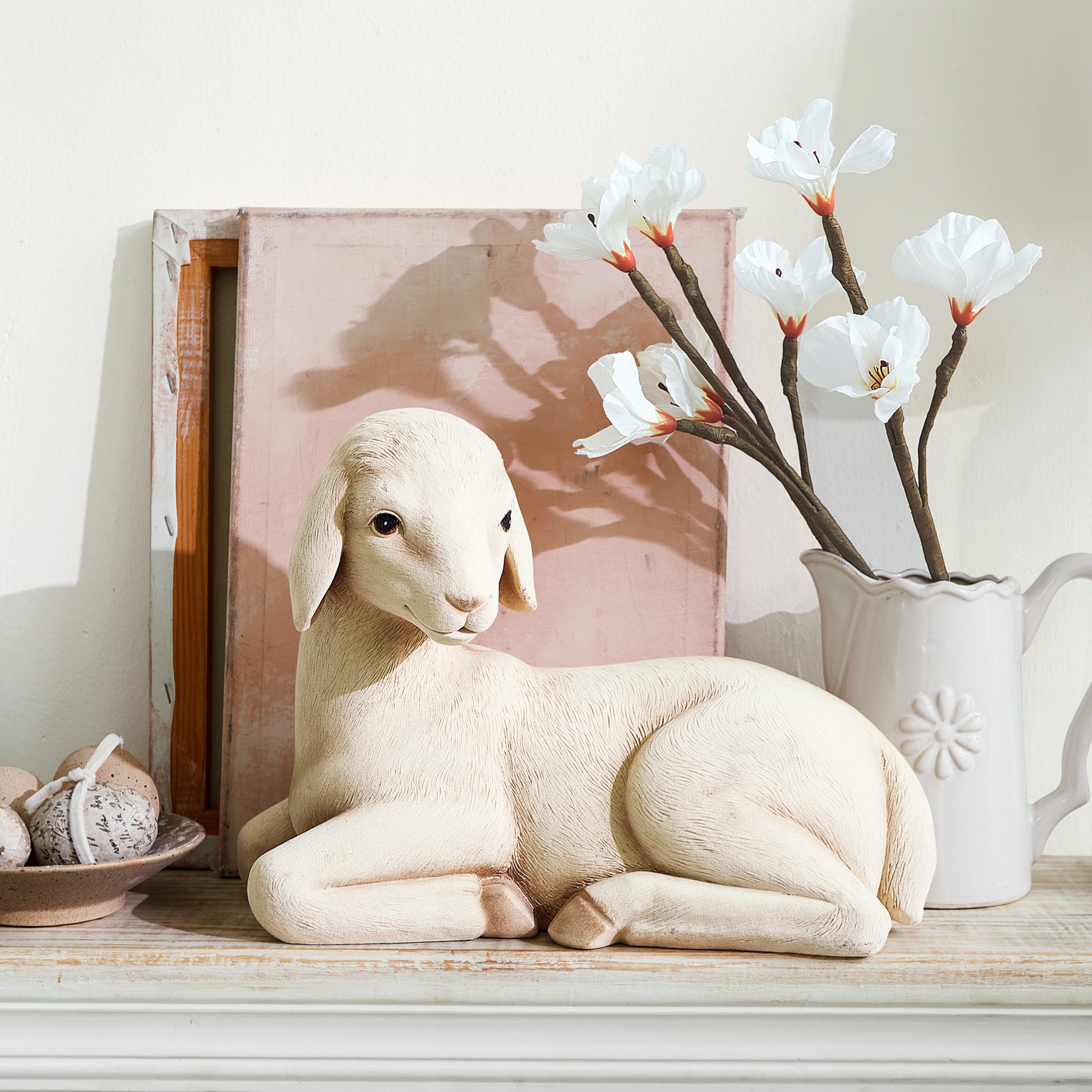 Figura decorativa di pecora chiara su mensola in legno con fiori bianchi e decorazioni