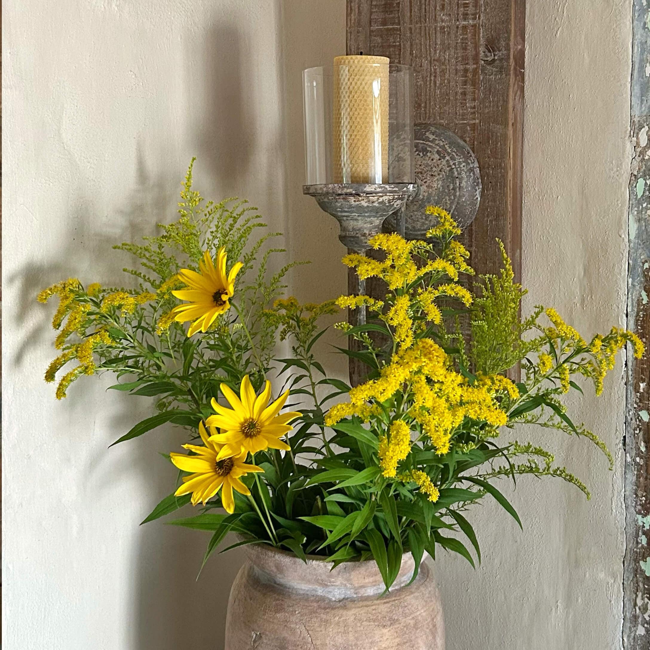 Fiori gialli in un vaso di terracotta davanti a una parete con un portacandele rustico