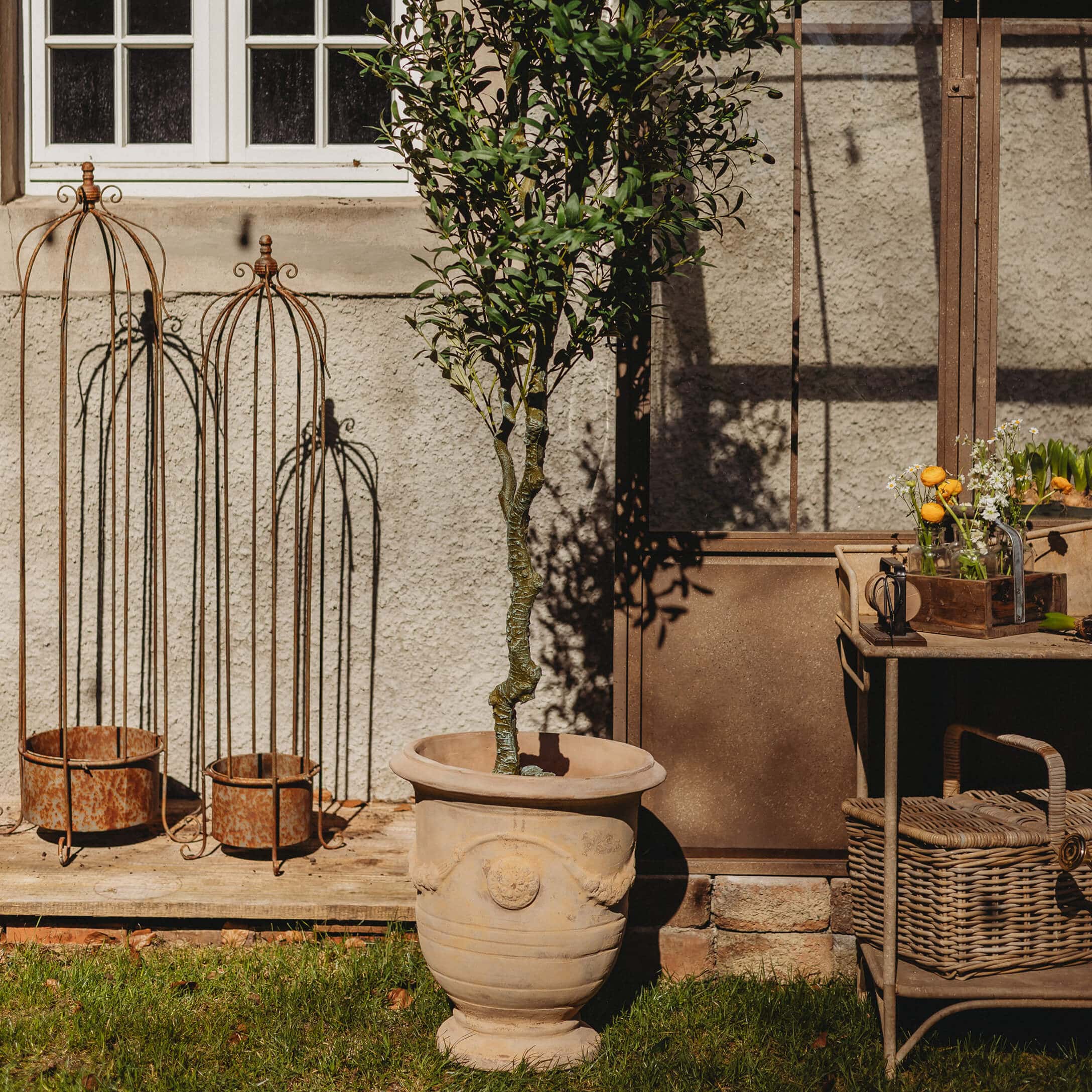 Grande vaso in ceramica beige con albero verde in giardino con decorazioni metalliche arrugginite