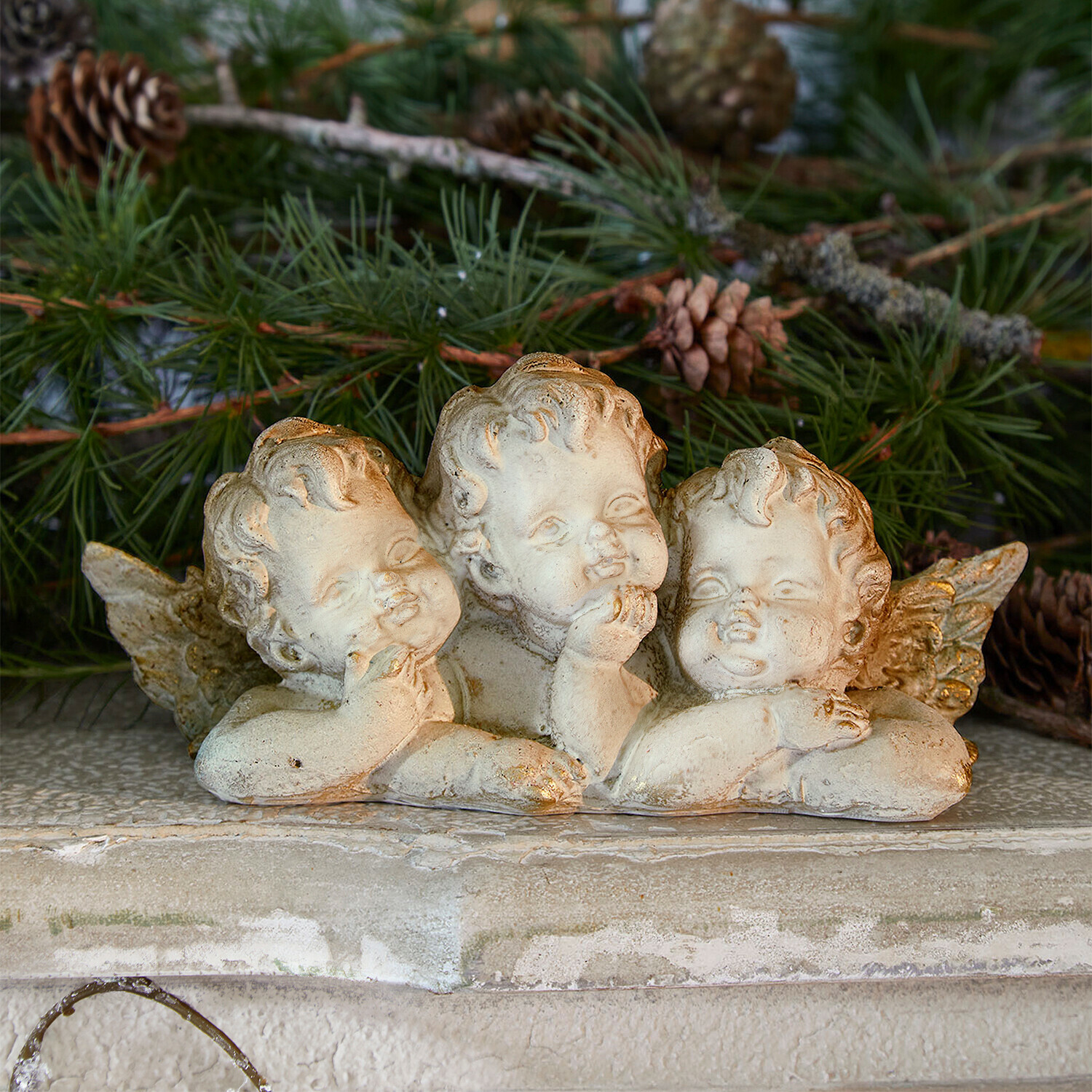 Angioletti decorativi Nivardo Figura di tre angeli in pietra chiara su sfondo di rami di pino verdi, decorazione natalizia