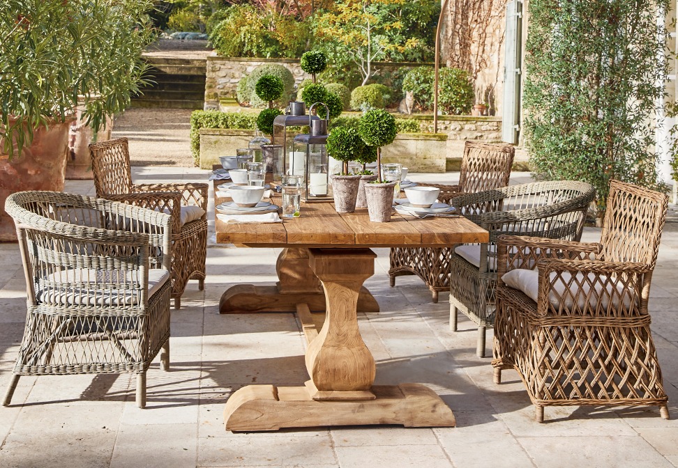 Tavolo da giardino in legno con sedie in vimini e decorazioni vegetali su terrazza in stile mediterraneo