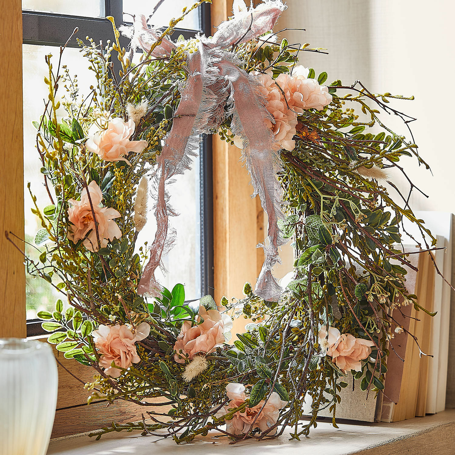 Ghirlanda Chérisse Corona decorativa di rami, fiori rosa e foglie verdi con nastro rosa sulla finestra