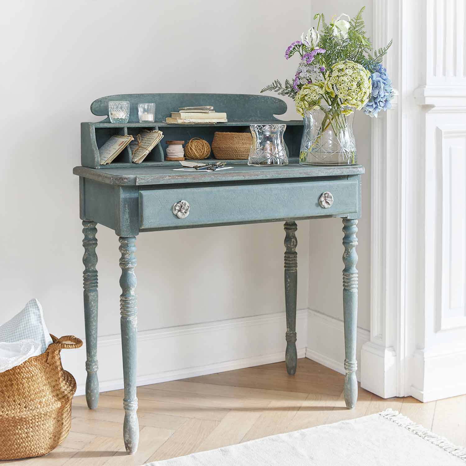 Scrivania in legno blu con cassetto e ripiani, decorata con vaso di fiori e candele