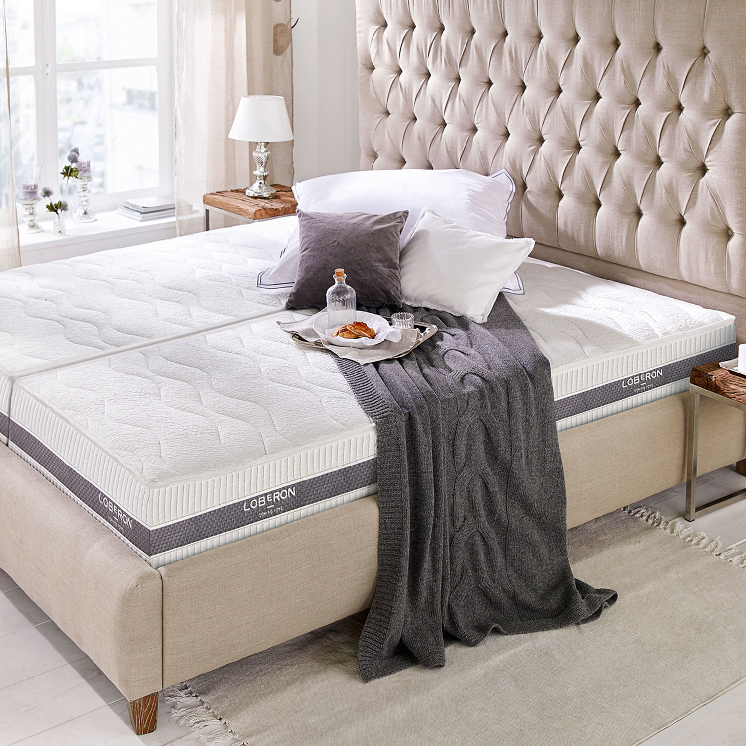 Materasso 90x200 Sevilha Letto imbottito beige con materasso bianco Loberon, coperta grigia e cuscini in camera luminosa