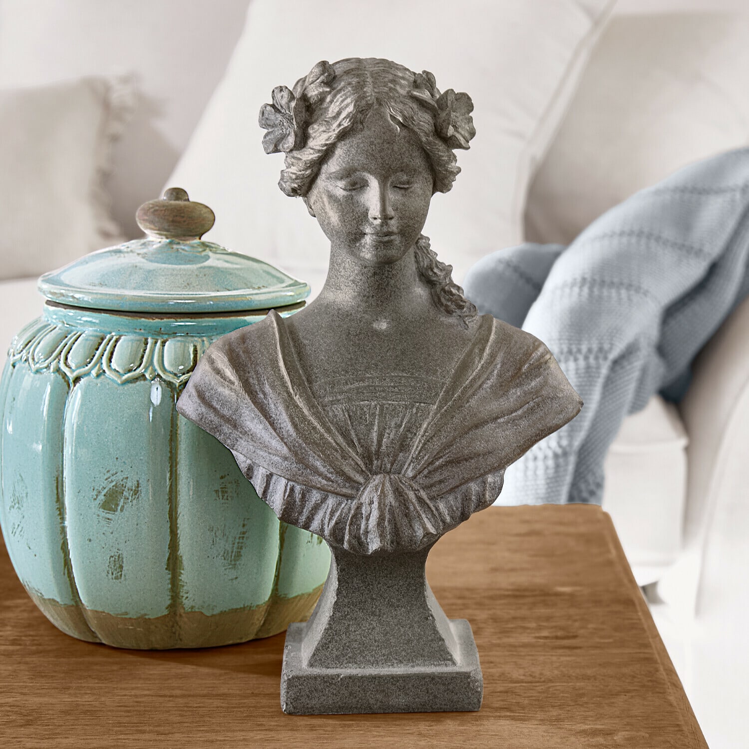 Busto Alexandra Busto femminile in pietra grigia con fiori tra i capelli su tavolo in legno accanto a vaso ceramico turchese