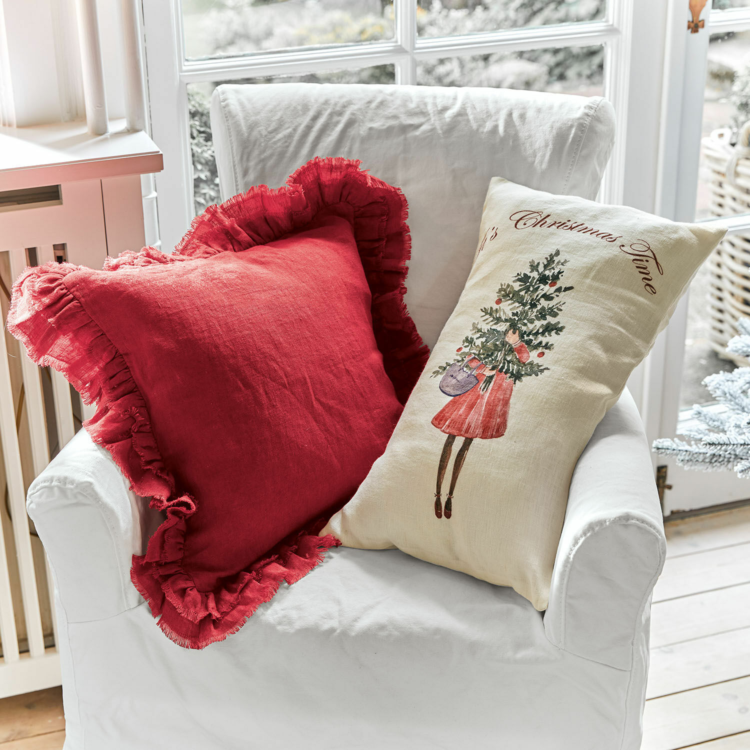 Coppia di copricuscini Christmas Time Due cuscini decorativi in lino su poltrona bianca, rosso con volant e crema con motivo natalizio