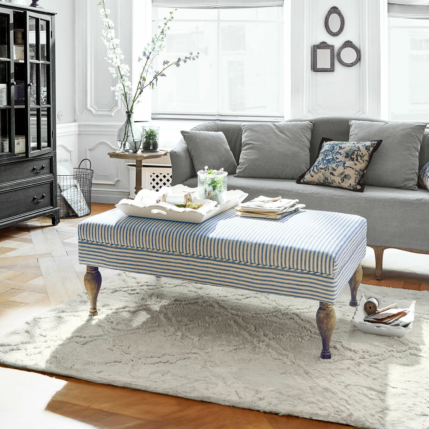 Pouf Ulysette Pouf a righe con gambe in legno su tappeto chiaro in soggiorno moderno con divano grigio