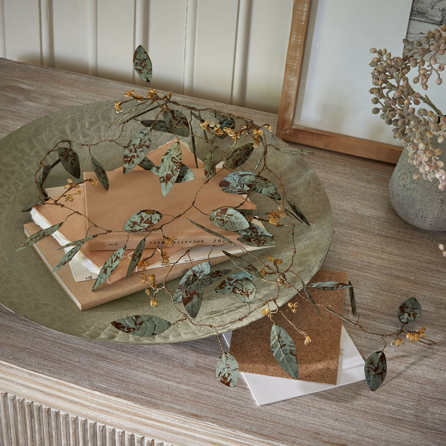 Festone Florivine Ramo decorativo in metallo con foglie verdi e bacche gialle su tavolo in legno con libri