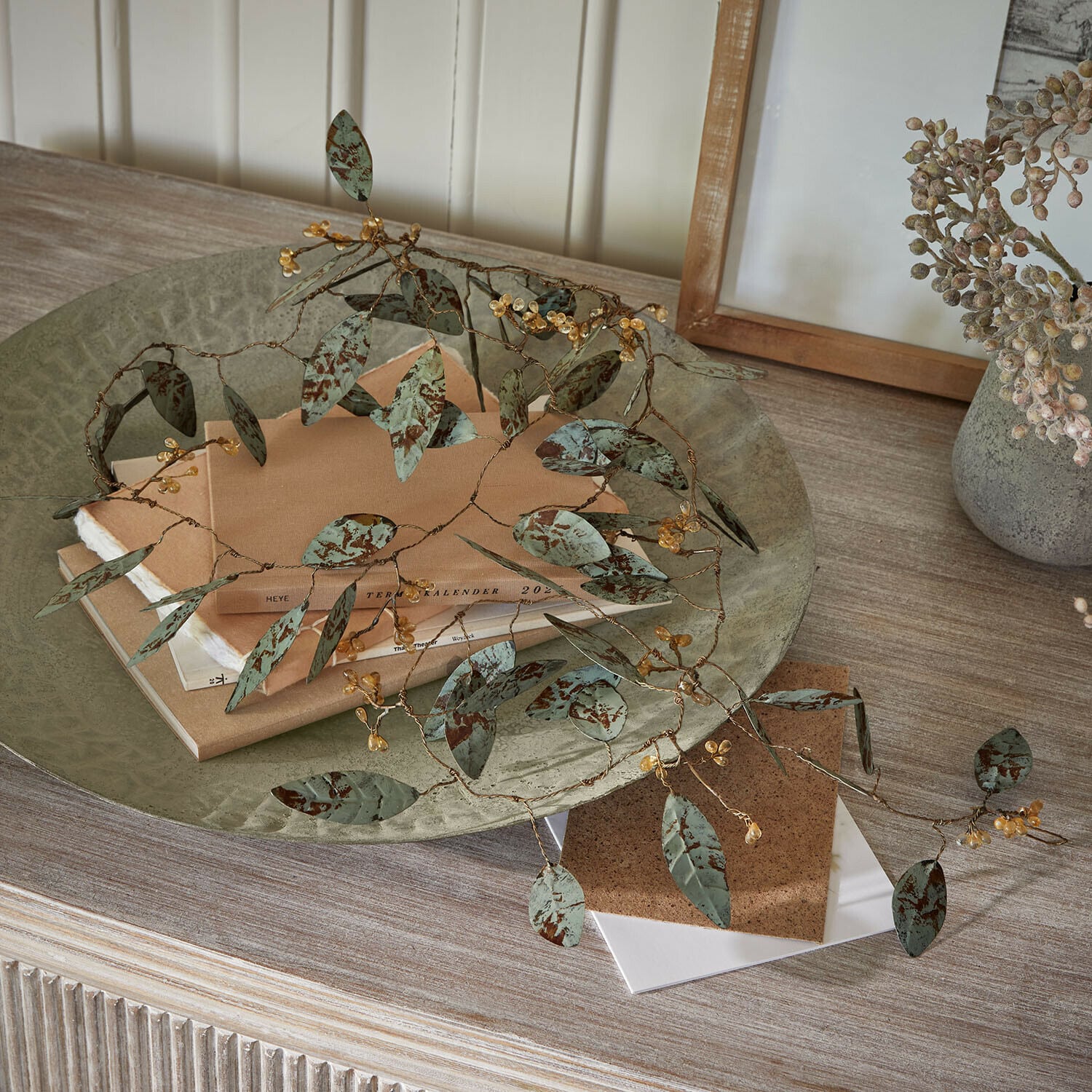Festone Florivine Ramo decorativo in metallo con foglie verdi e bacche gialle su tavolo in legno con libri