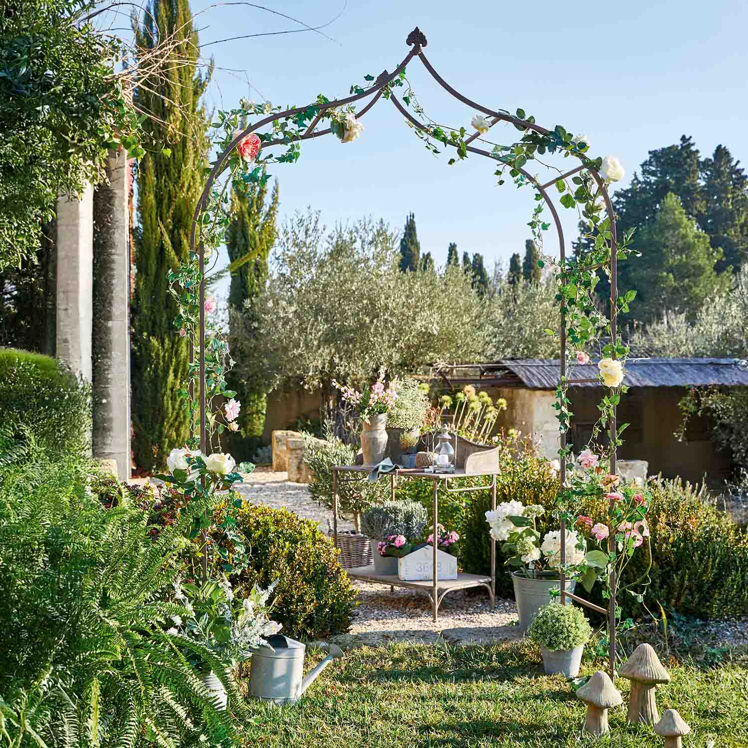 Pergola da giardino in metallo con foglie verdi e fiori rosa in giardino soleggiato
