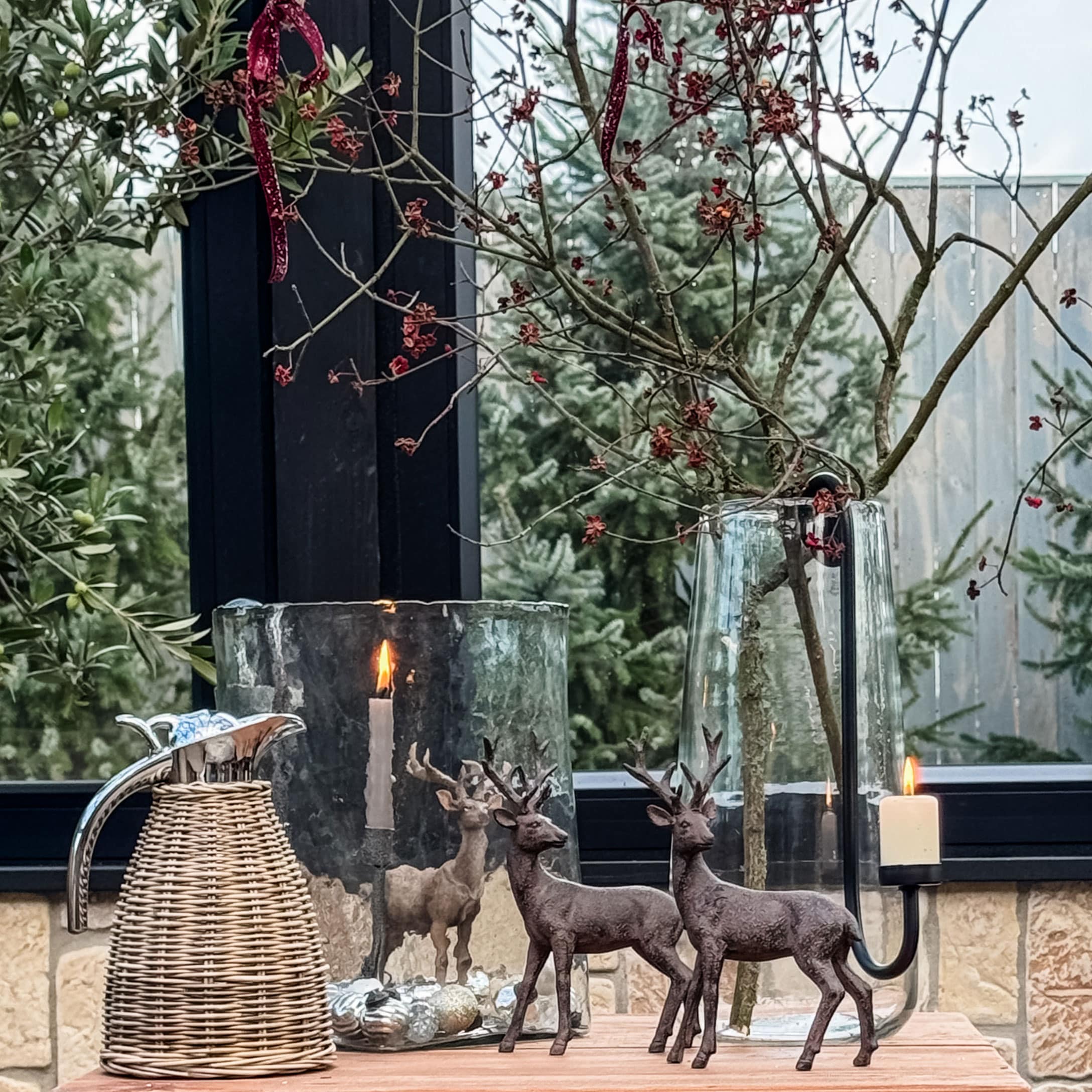 Decorazione natalizia con due figure di cervi marroni, portacandele in vetro e brocca in rattan