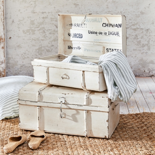 Bauletti in legno bianco vintage con tessuti a righe e pantofole su tappeto di juta