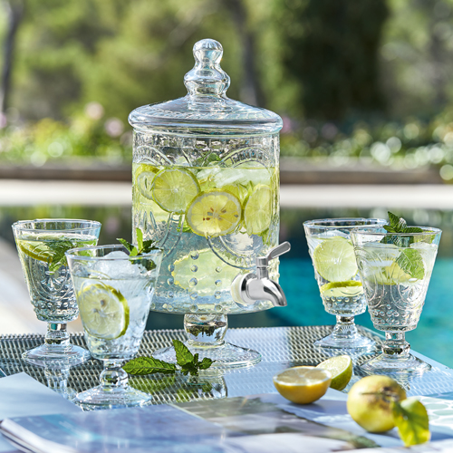 Dispenser di vetro con limone e menta, quattro bicchieri su tavolo esterno vicino alla piscina