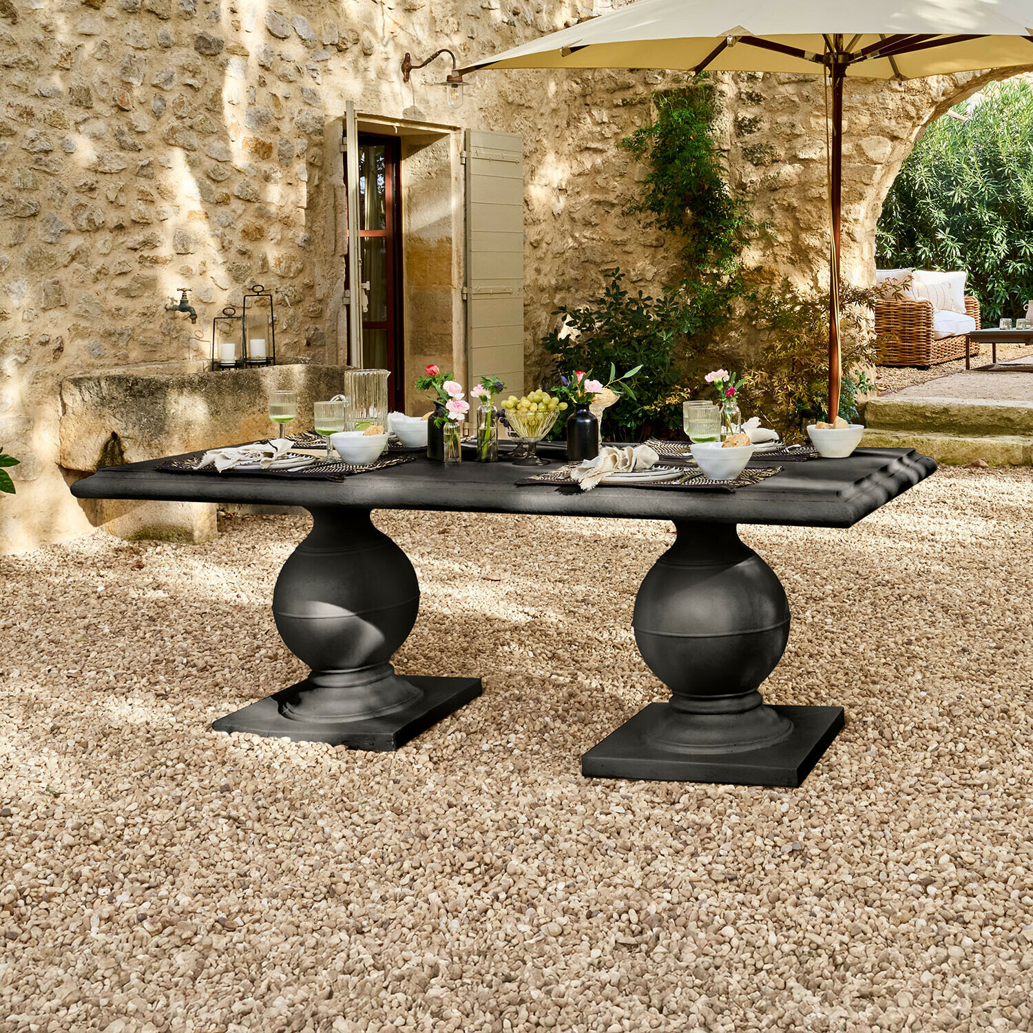Tavolo Talvero Tavolo da giardino nero in pietra con due gambe sferiche su patio di ghiaia sotto ombrellone