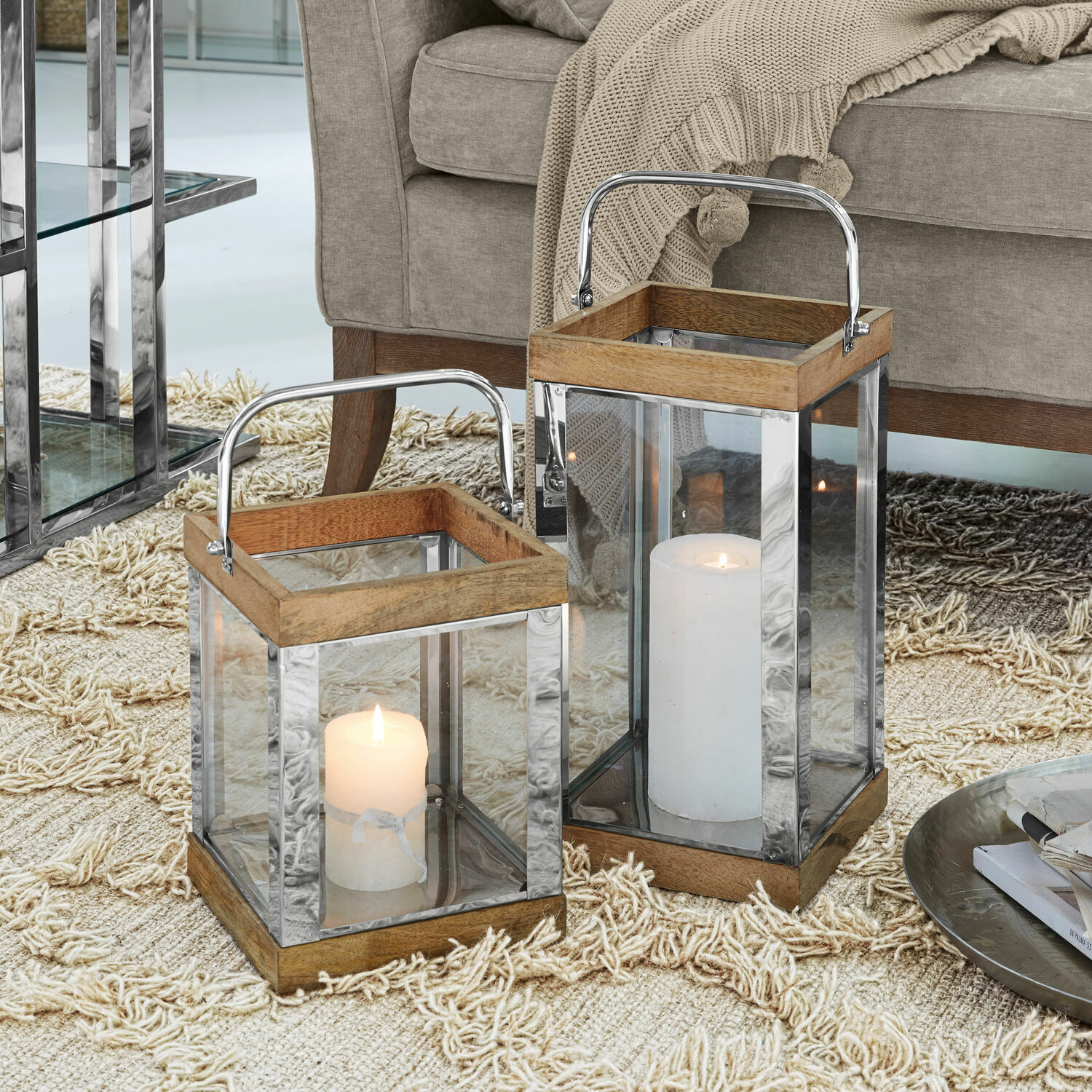 Coppia di lanterne Harpers Due lanterne in legno e metallo con pareti in vetro e candele bianche su tappeto beige
