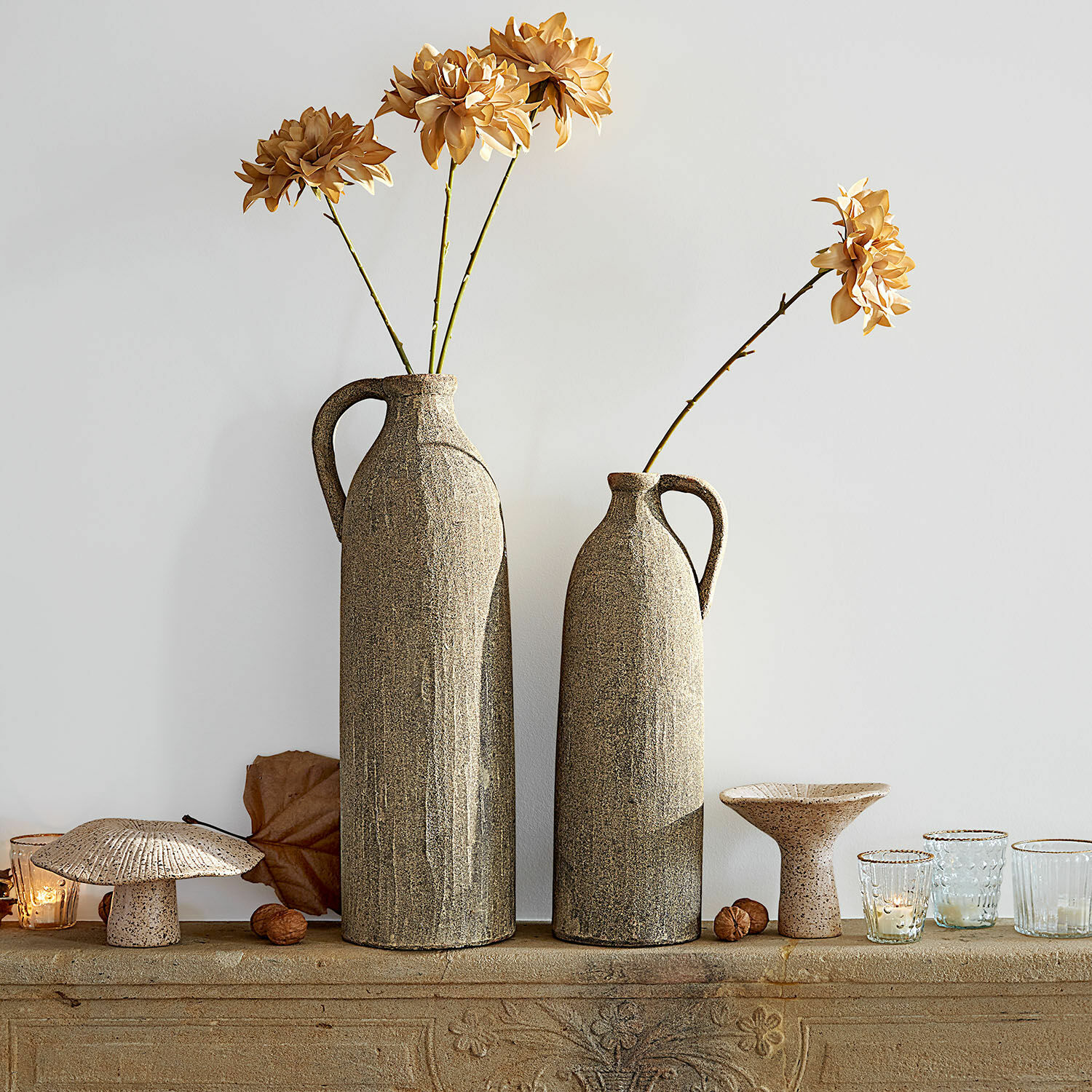 Coppia di vasi Kalidaan Due alti vasi in ceramica beige con fiori secchi e decorazioni su una mensola in pietra