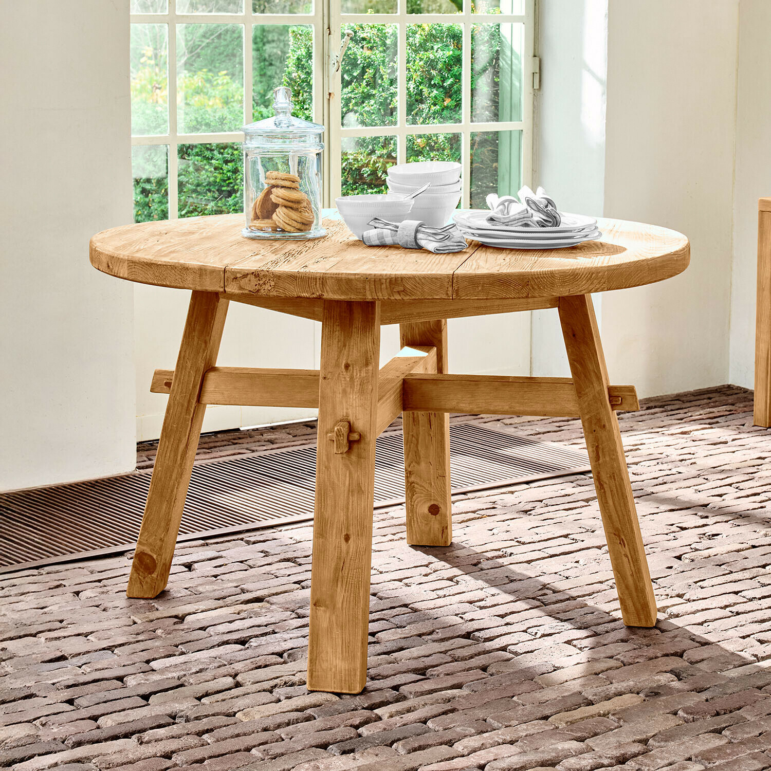 Tavolo rotondo in legno di pino naturale su pavimento in mattoni vicino a finestra luminosa