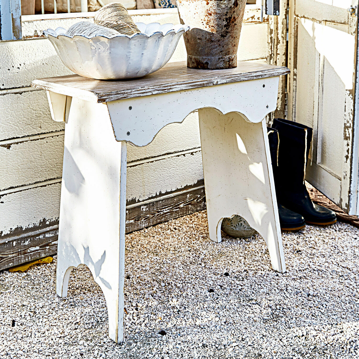 Sgabello Fria Tavolino in legno bianco effetto invecchiato su ghiaia con ciotola decorativa e stivali neri