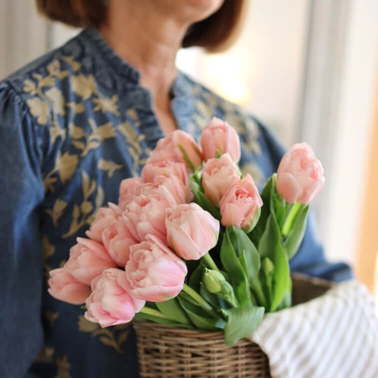 Mazetto di tulipani rosa in cesto di vimini tenuto da donna con camicetta blu a fiori