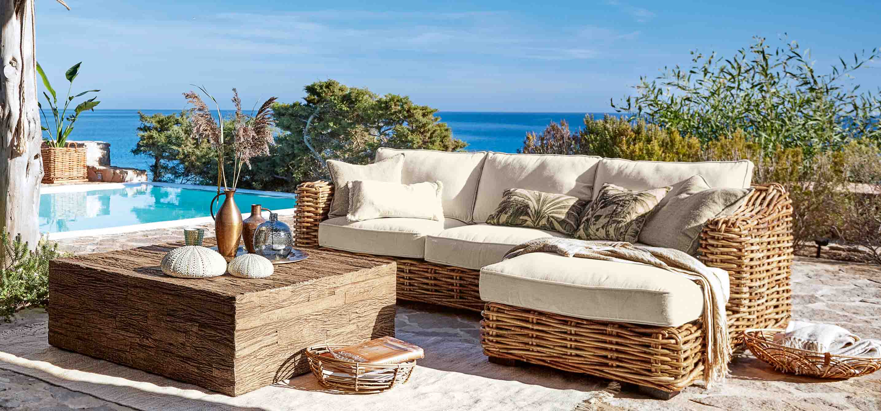Set di mobili da giardino in rattan con cuscini crema vicino a piscina con vista mare