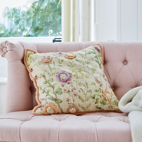 Cuscino decorativo con ricamo floreale in colori pastello su divano rosa, tessuto morbido