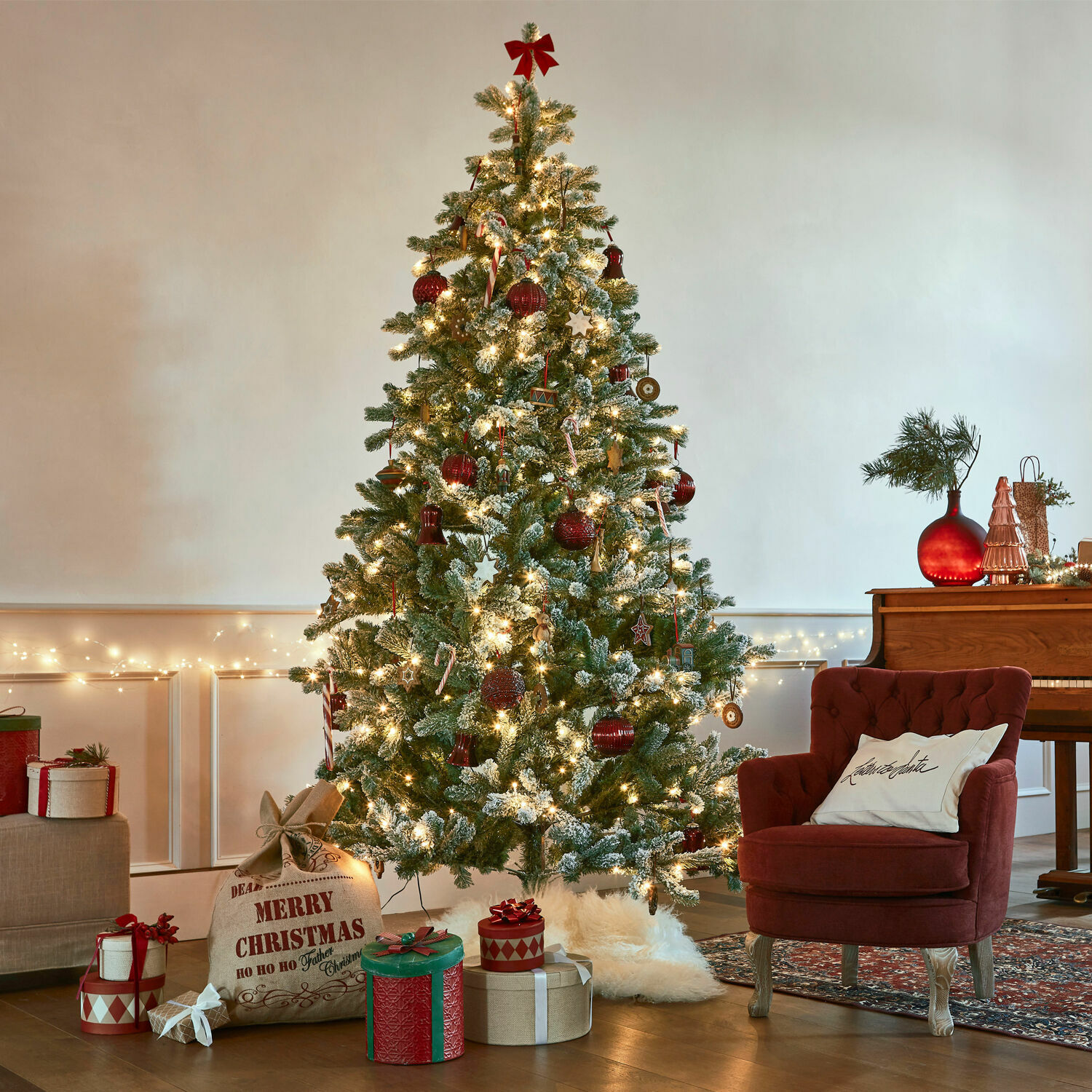 Albero di Natale Mannier Albero di Natale artificiale innevato con decorazioni rosse e luci in un soggiorno accogliente
