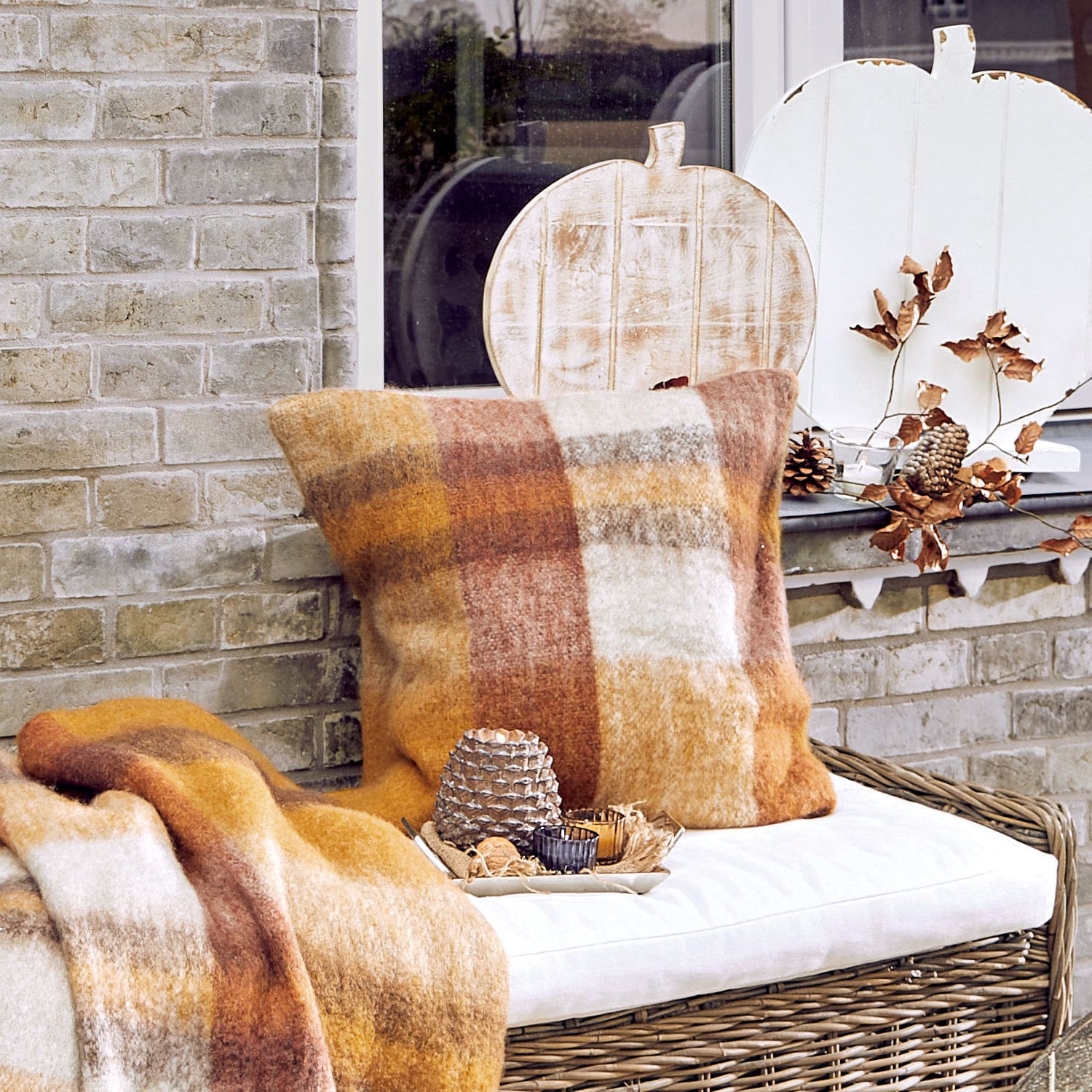 Copricuscino Cabiate Cuscino e coperta in tonalità calde marroni e beige su panca in vimini con decorazioni autunnali