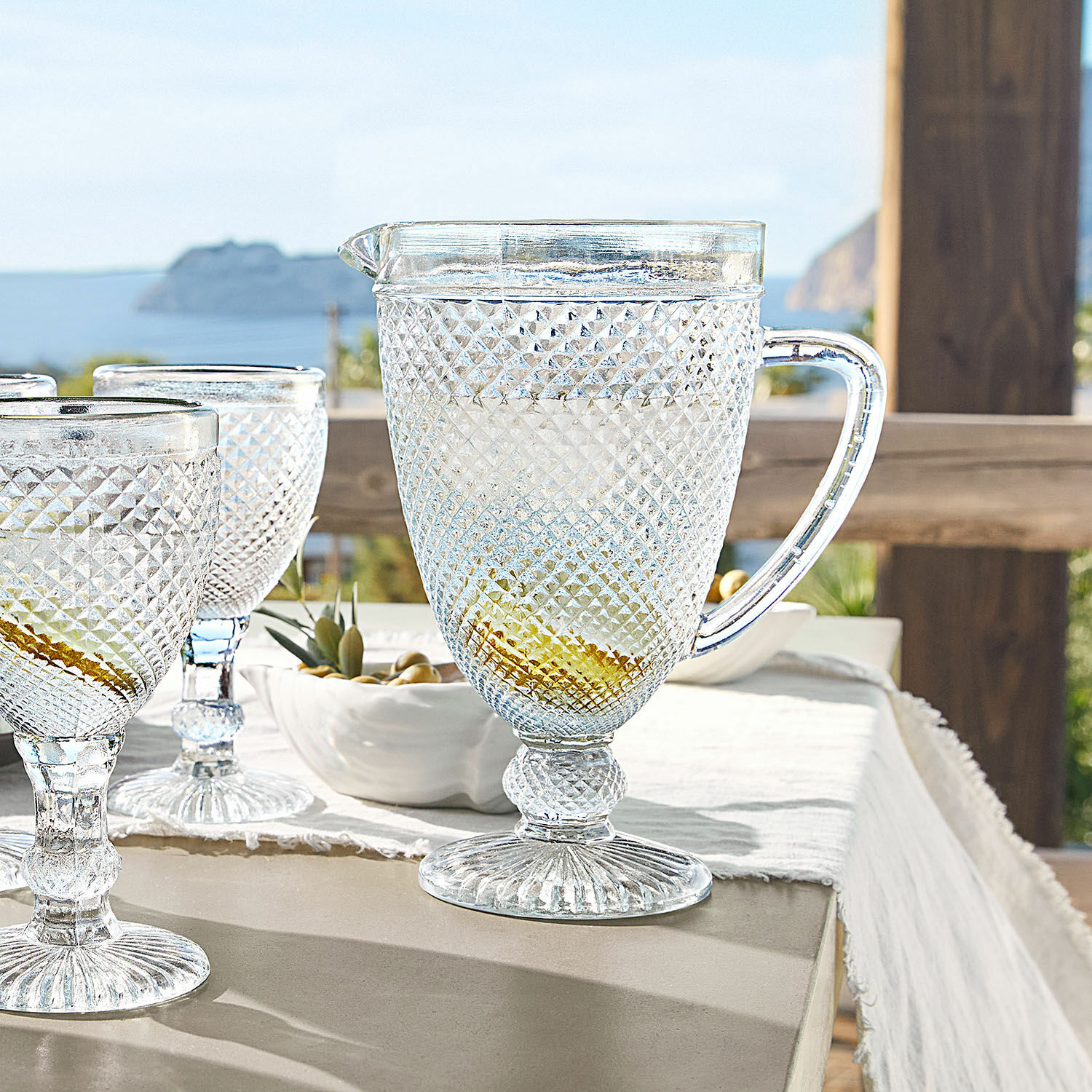 Caraffa Santerre Caraffa e bicchieri trasparenti in vetro con motivo a rilievo su tavolo con vista mare