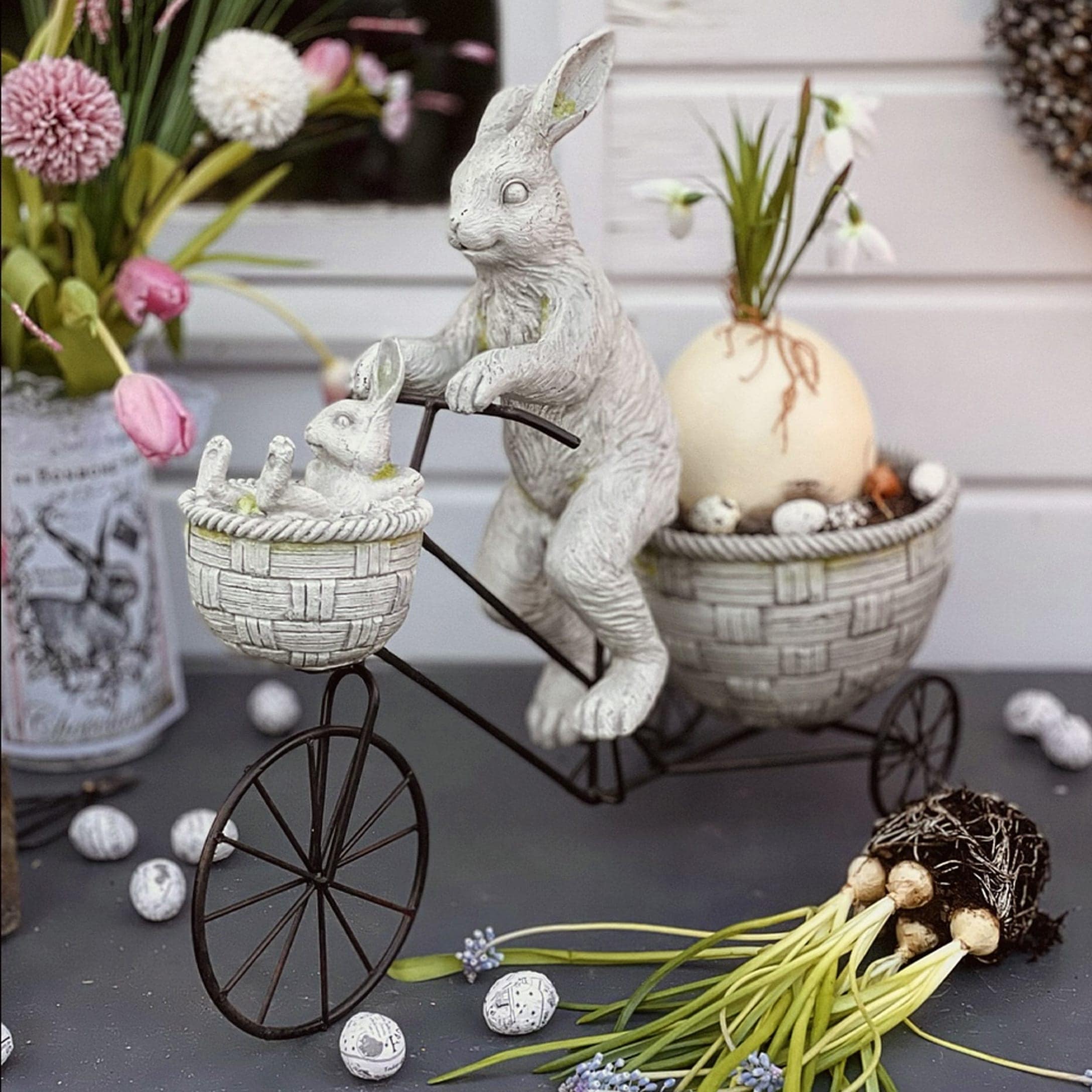Decorazione pasquale con conigli bianchi in resina su bicicletta in metallo con cestini e fiori
