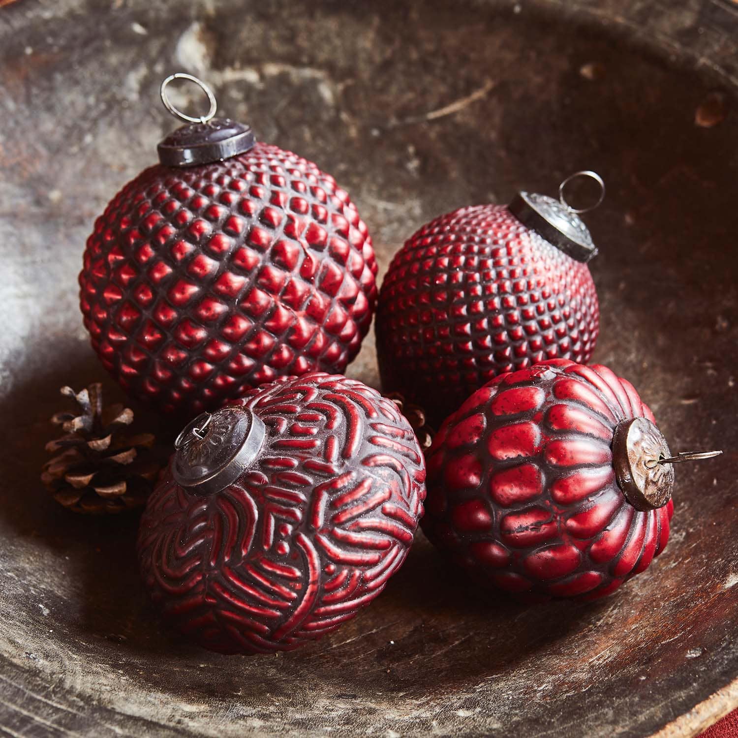 Quattro palline di Natale rosse con diverse texture in una ciotola di legno con pigne