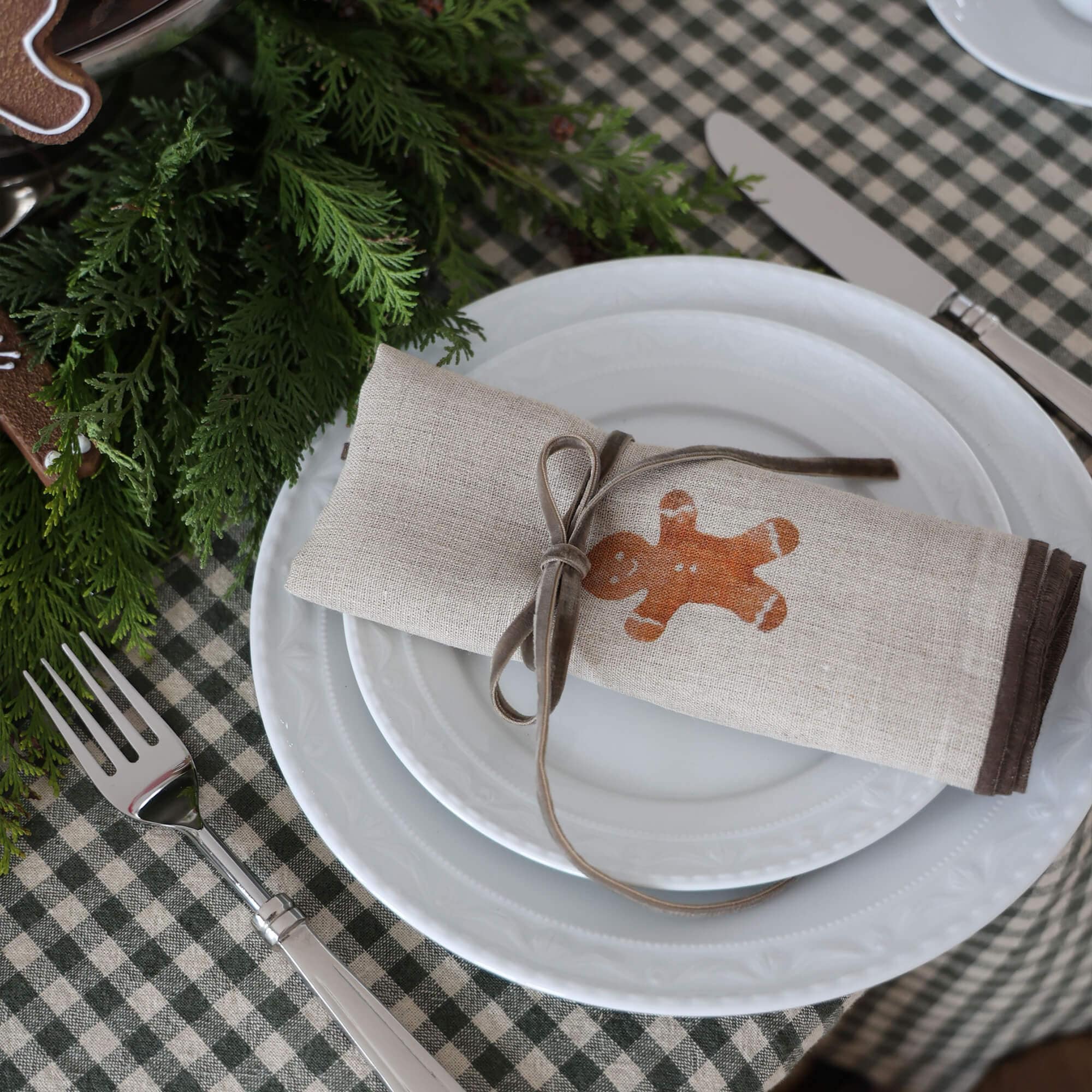 Tovagliolo in lino beige con stampa omino di pan di zenzero e nastro grigio su piatto bianco