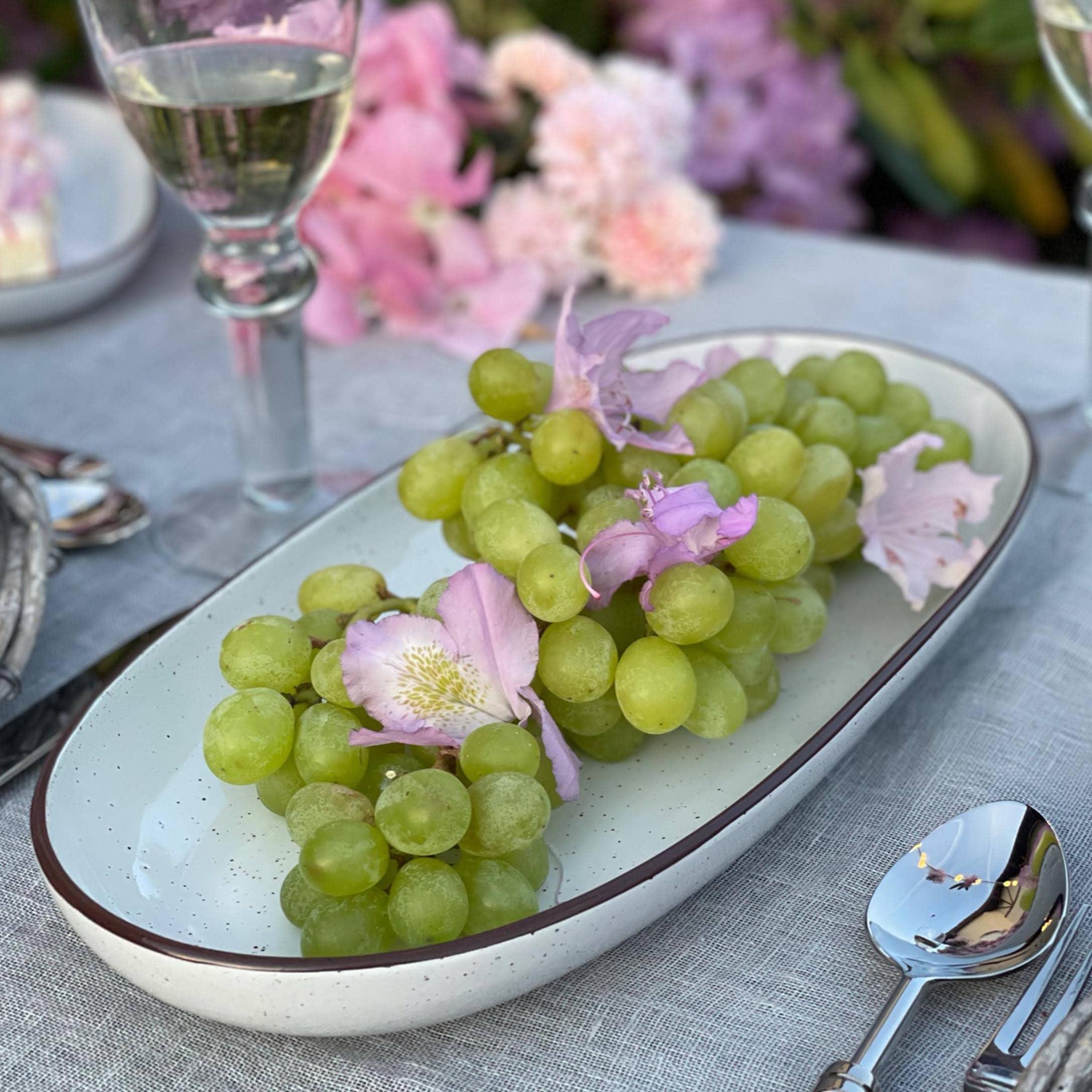 Uva verde con fiori rosa su piatto in ceramica bianca su tovaglia grigia